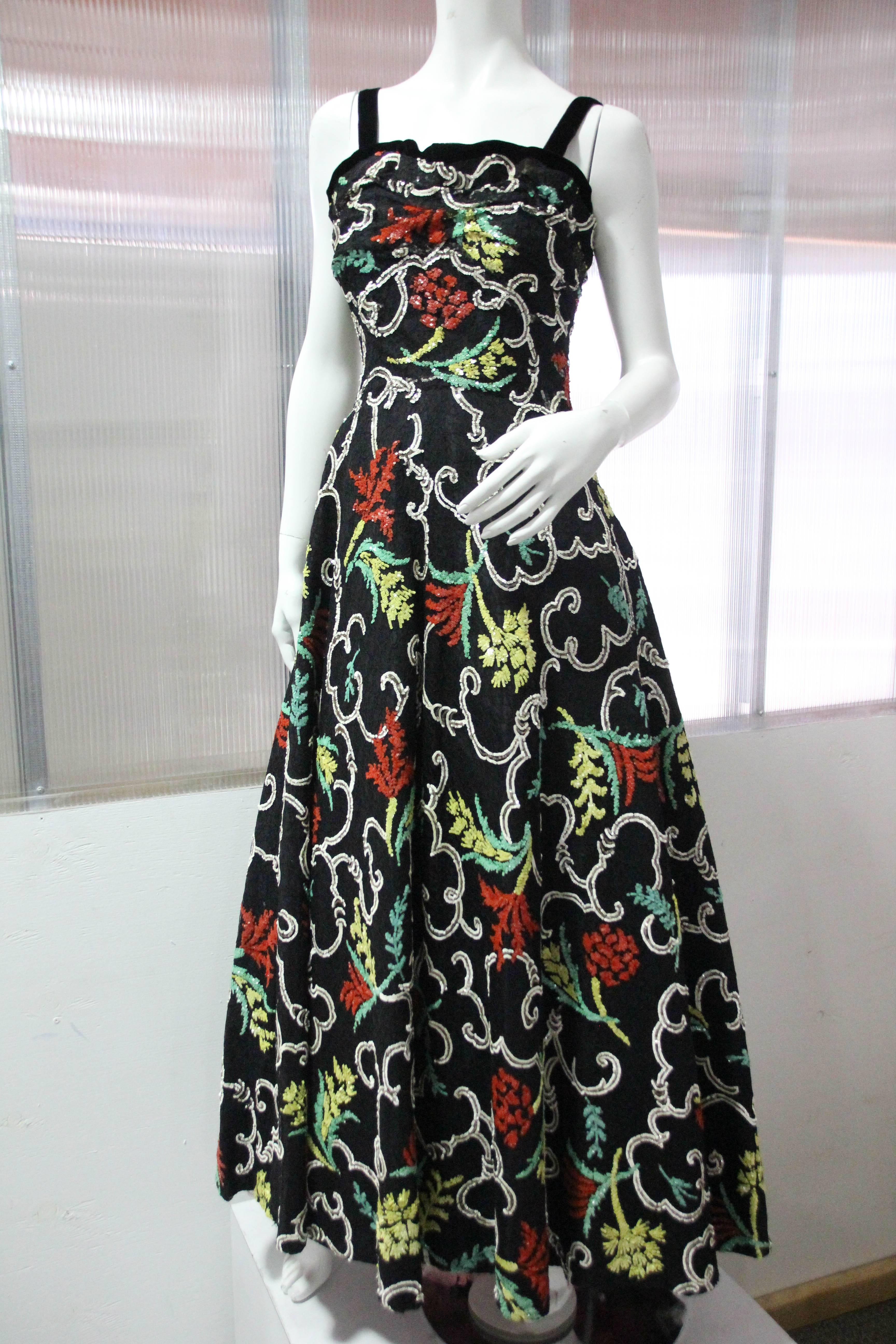 This exquisite late 1930s couture gown is unmarked as to maker, however, it is undoubtedly of the highest quality: The black silk lace is trimmed with velvet at straps and decolletage and is covered entirely with a beautiful, hand-sewn green, white,