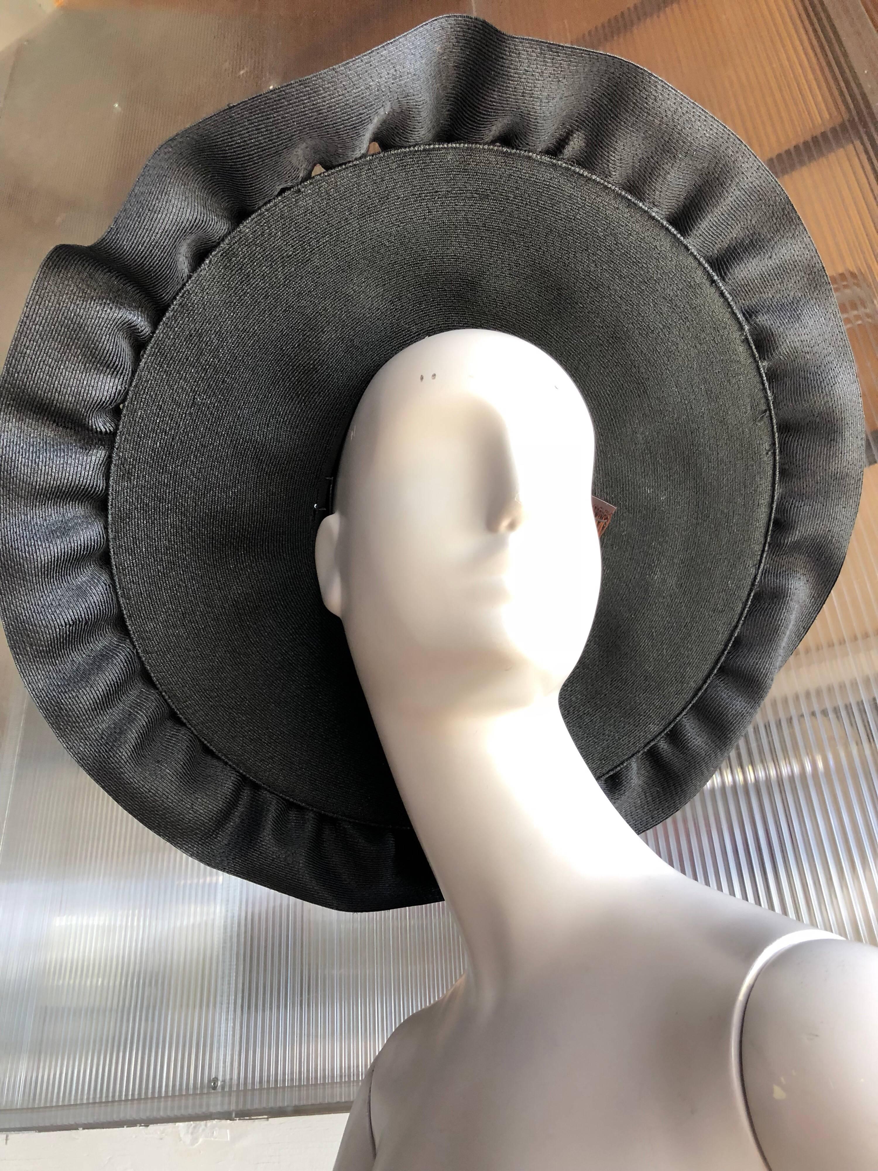 A 1940s Irina Roublon large and dramatic black straw hat with ruffled straw at brim and steel blue satin lining inside crown.  Crown opening is small and is meant to perch on head and be secured with 3 original attached combs, not to be worn fitted