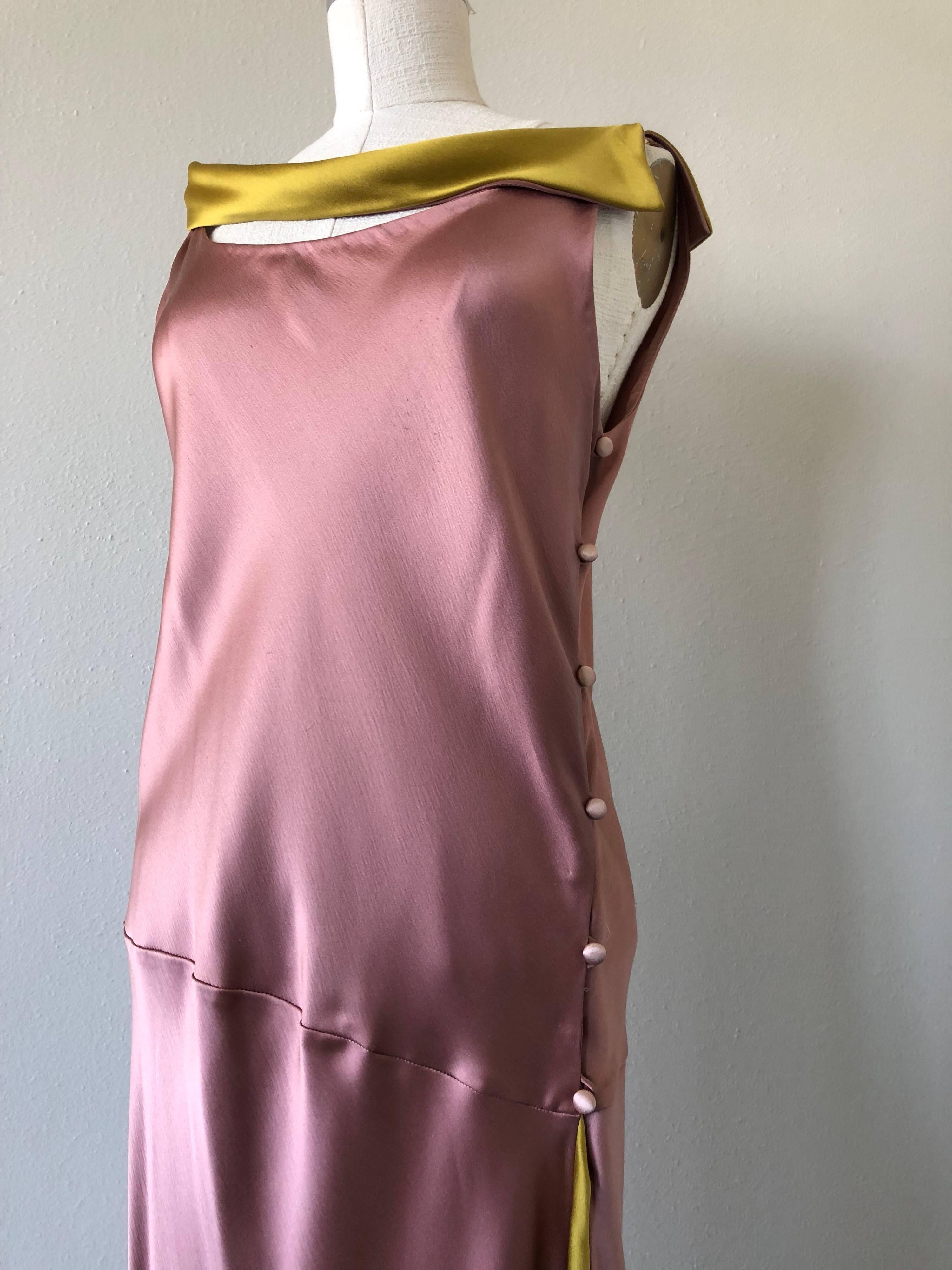 A gorgeous 1990s Bill Blass 2-tone silk charmeuse dress in mauve and burnished gold:  Bias cut with buttons down the side, this beautiful dress features a burnished gold satin side-slung collar piece and an inset flared panel  at the side. 