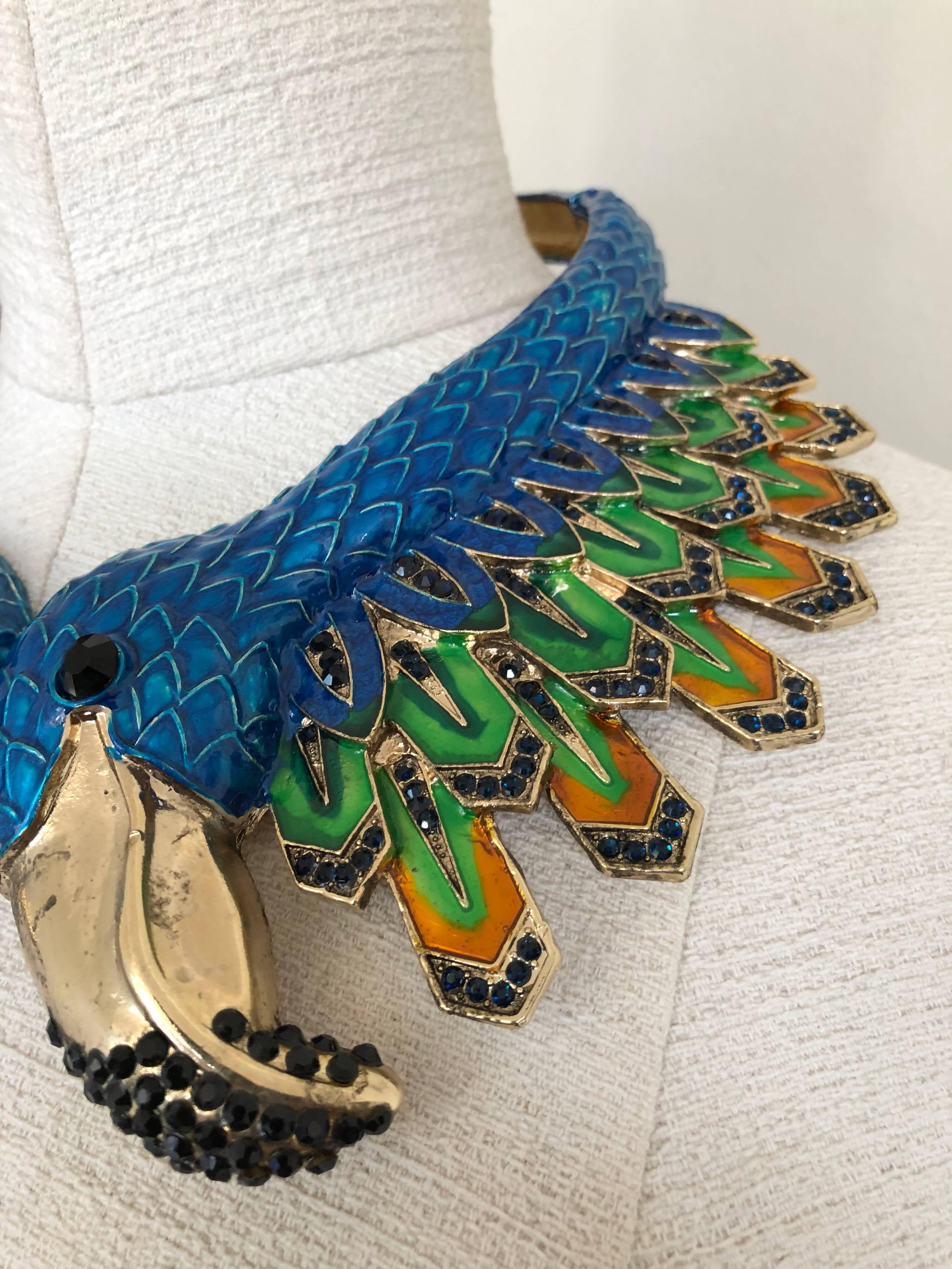 A bold 1980s Azure blue enameled deco style exotic bird hinged collar necklace features lifelike feather details and black crystal speckles throughout the entire collar design.
This very heavy hinged collar allows one to slide the necklace on with