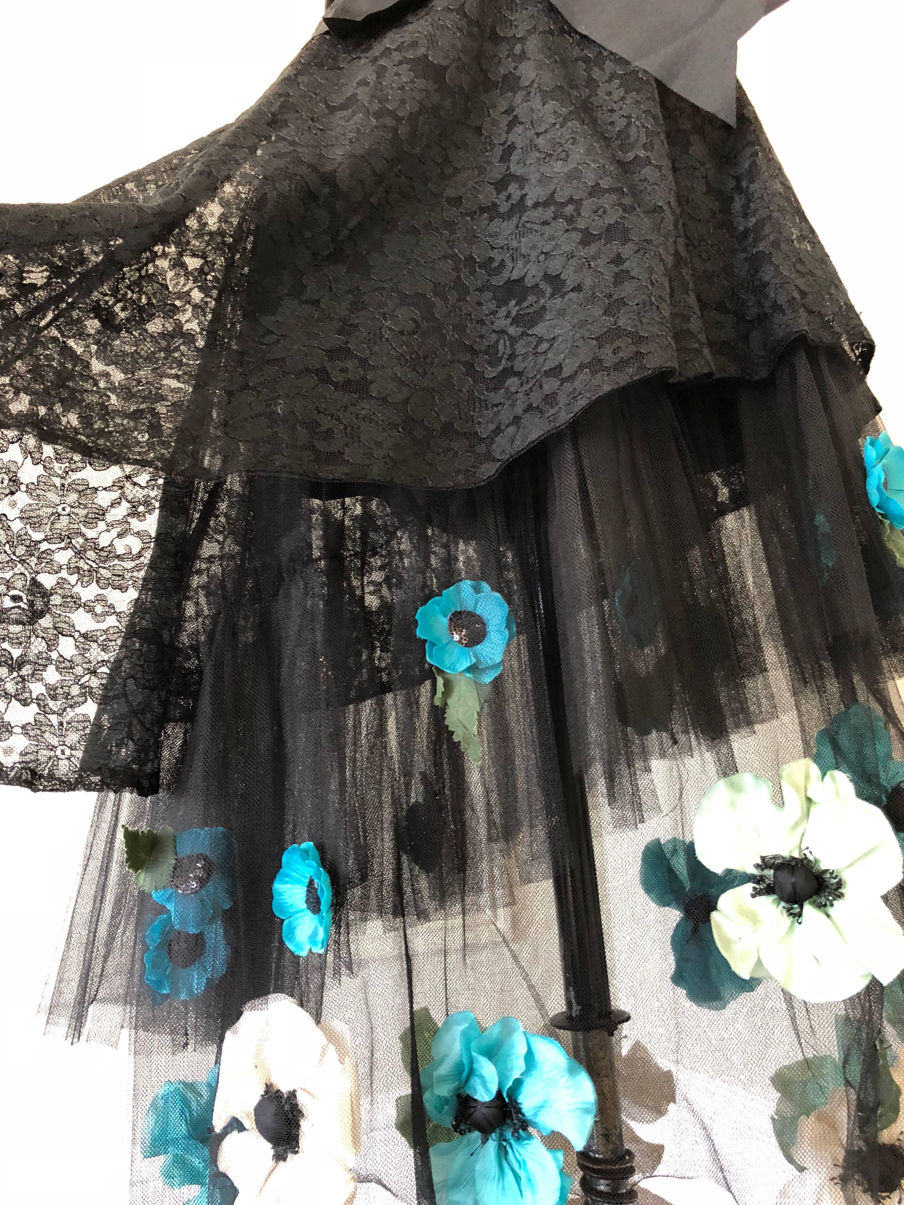 A 1950s style black lace and tulle skirt ensemble features a wonderful color combination of silk flowers arranged throughout the assymetrical skirt hemline. The large grosgrain ribbon wraps around the waist forming a bow tie. Coordinating black