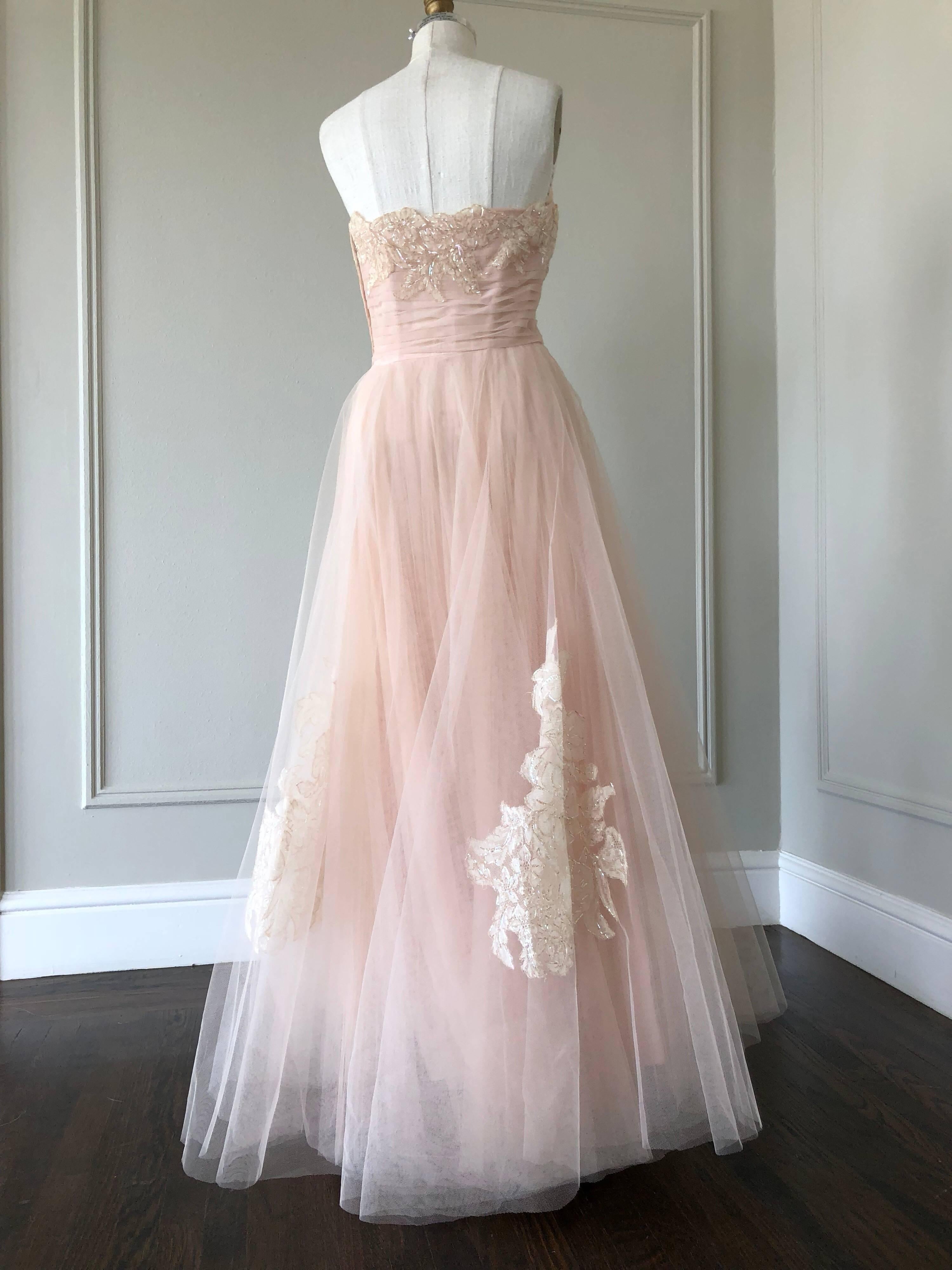 A gorgeous 1950s evening gown in pink champagne tulle with lace and sequin applique at skirt and bodice.  Boned and structured bodice is strapless.  Skirt is layered with three tulle tiers, one of which is completely pleated. 
