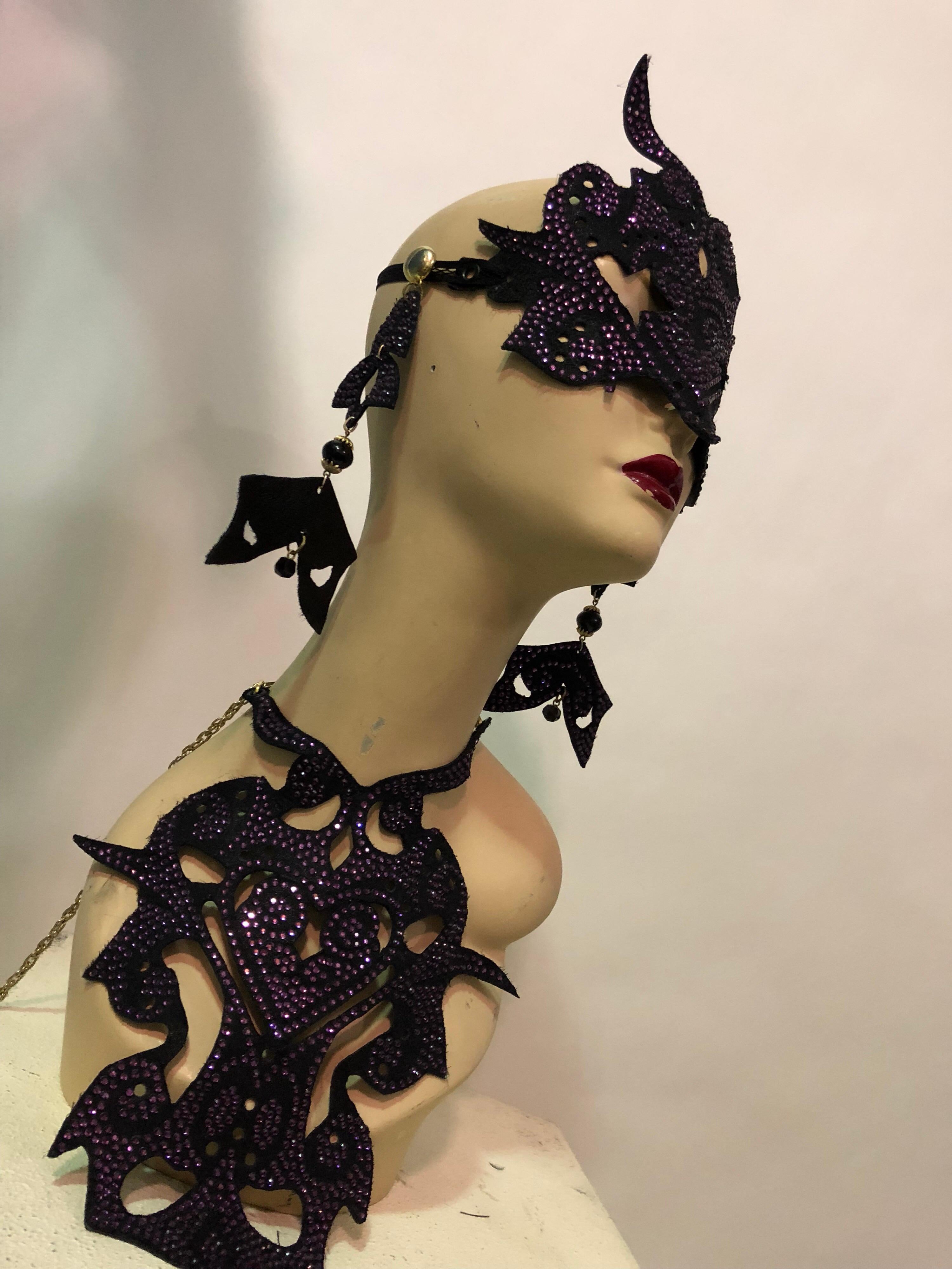 An avant garde custom made 3-piece leather mask ,earrings and bib necklace with purple crystals. Earrings are clip chandeliers. Bib collar is leather bound with tie at back. 
This ensemble is a striking look for any Masquerade Ball or Burning Man!