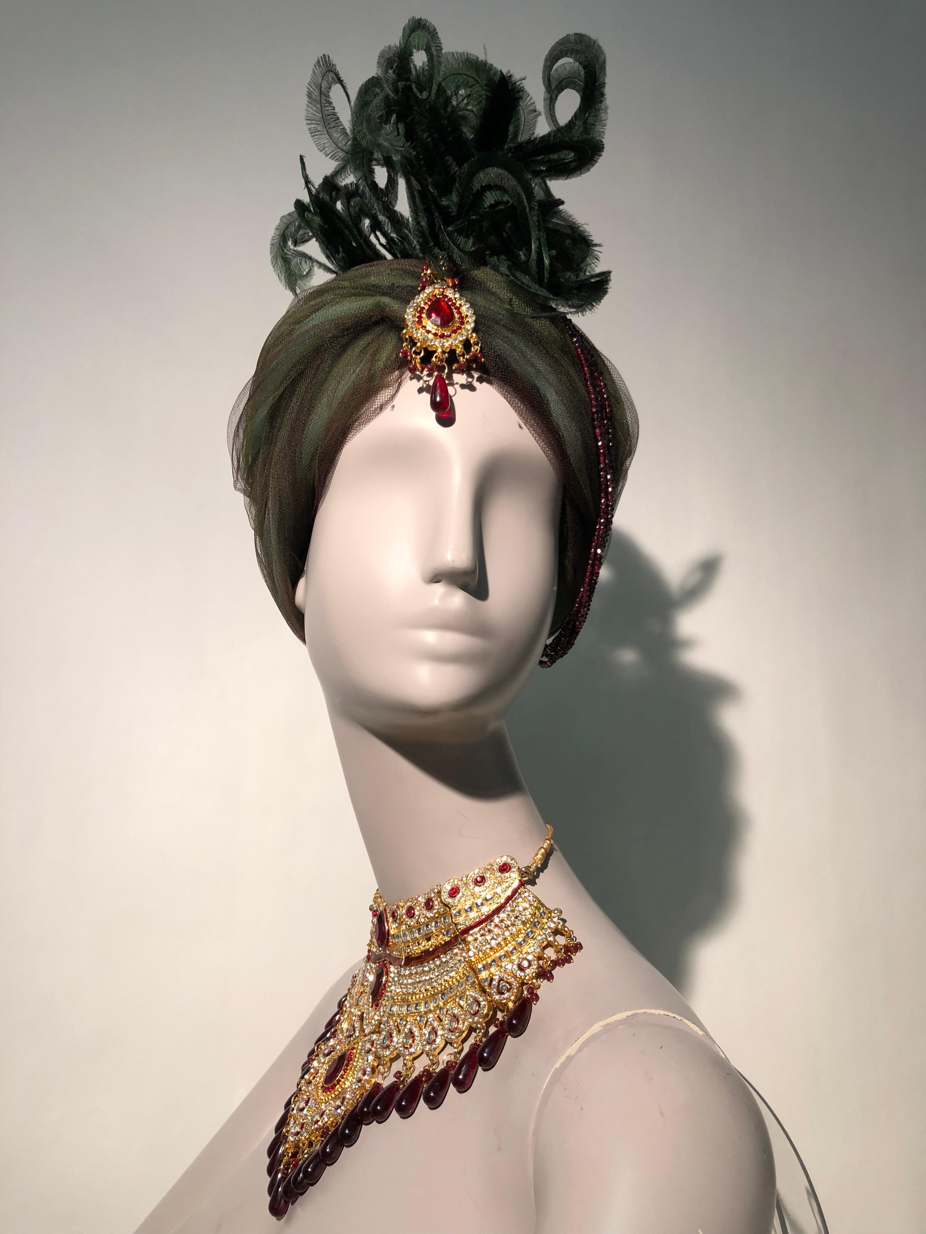 A gorgeous costume set: a 1960s Mr. Robert green and brown tulle turban hat with a spectacular crest of curled green feathers. Turban is jeweled at center front with crimson resin brooch. Five strands of genuine garnets are draped from center front