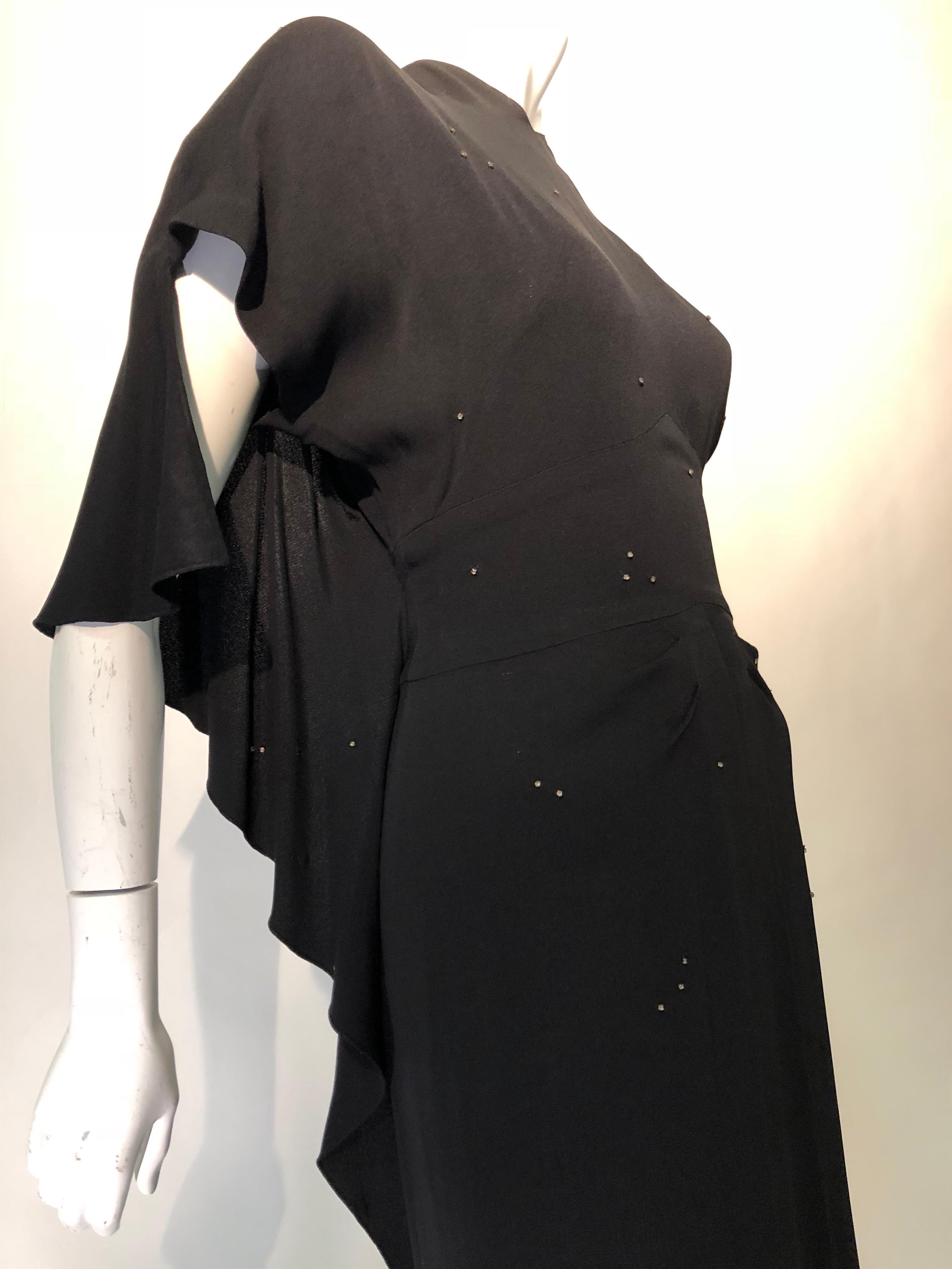 A rare mint condition 1940s Adrian evening gown of black silk crepe with dramatic draped back details, structured shoulders, fitted banded waist, back zipper, high V-neckline, pleated center-front drape and slit. In true Goddess style, this gown is