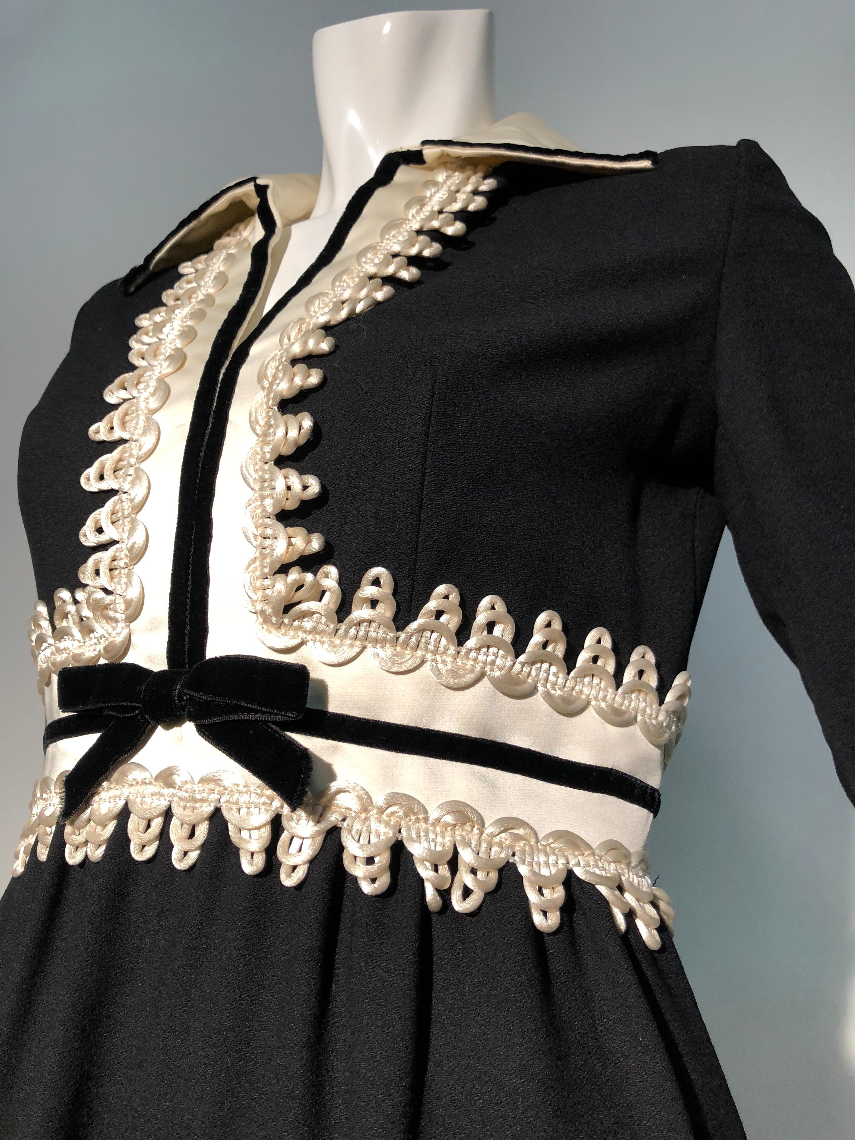 A fabulous 1960s Oscar de La Renta black wool crepe mini dress with fitted, inset white waistband and neckline. Neckline is embellished with ivory satin cord looped passimentery trim and a thin black velvet ribbon bow. Open collar. Back zipper. Side