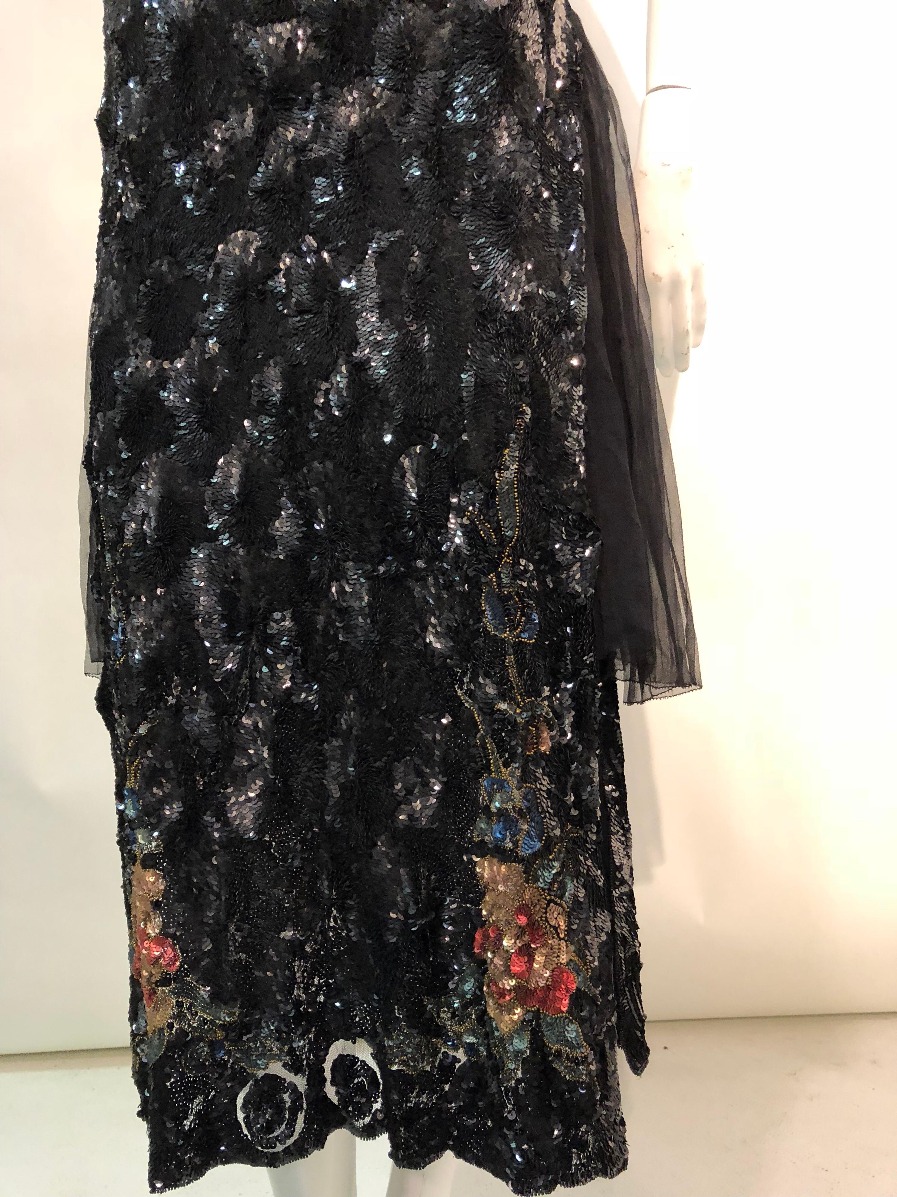 A lovely 1920s French-made tabard-style evening gown of silk tulle, heavily sequined in a whirl pattern and colored sequin flowers at top and hem. Side panels are gathered silk tulle. Back panel is fully lined, to give the drape weight to the back.