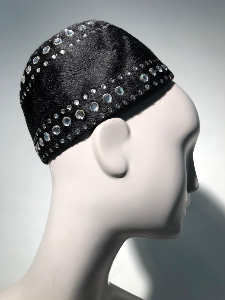 A wonderful 1960s Leslie James black felt hat to be worn at crown over a bun, chignon or such hairstyle. It is embellished all around with rows of glittering rhinestones. Original combs for secure attaching are present.