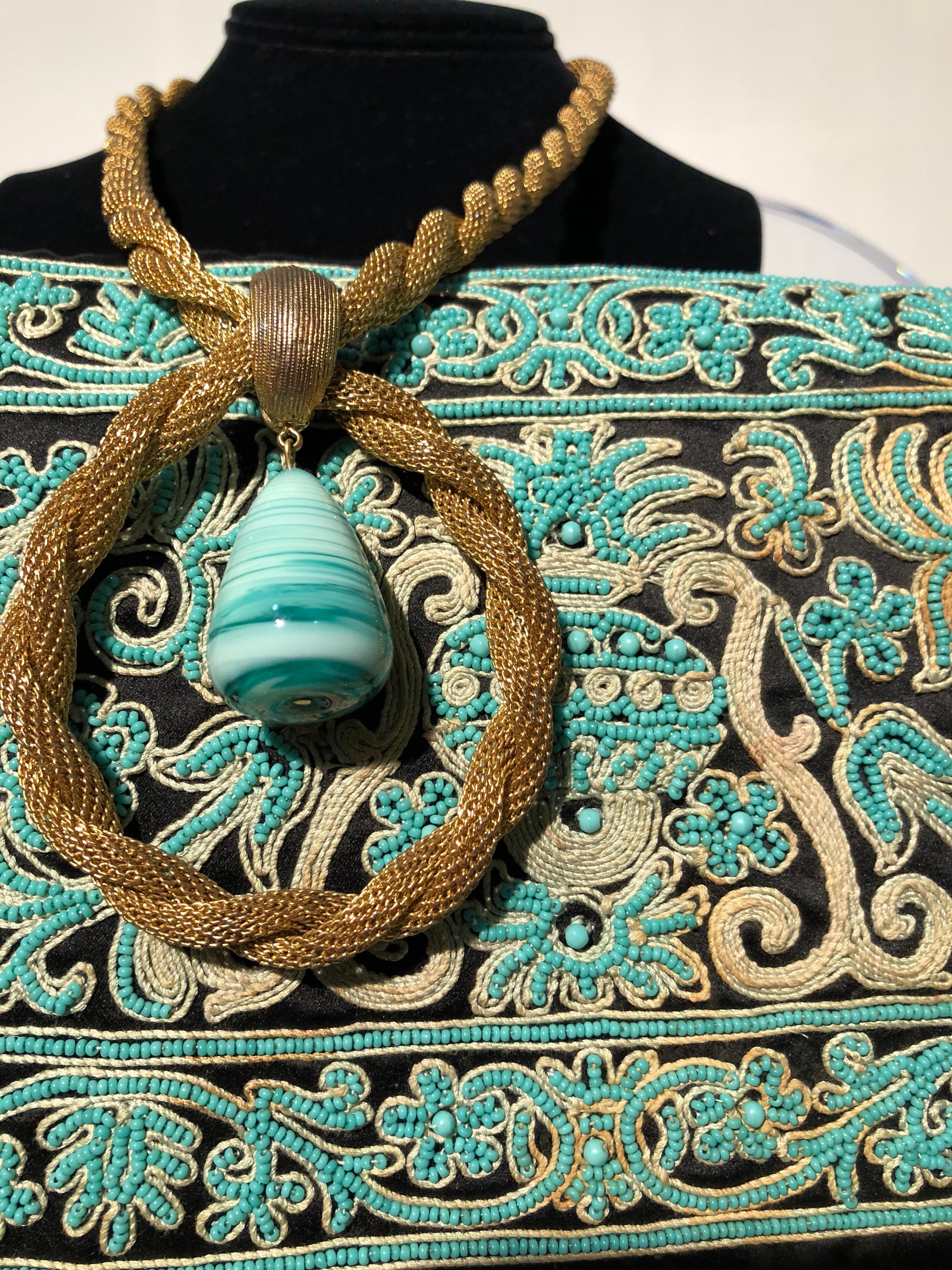 A lovely 1940s Henry Rosenfeld black satin envelope clutch purse with front heavily embroidered in traditional Indian style in turquoise and gold cording. A coordinating gold-tone metal rope necklace with slang glass drop pendant is included. 