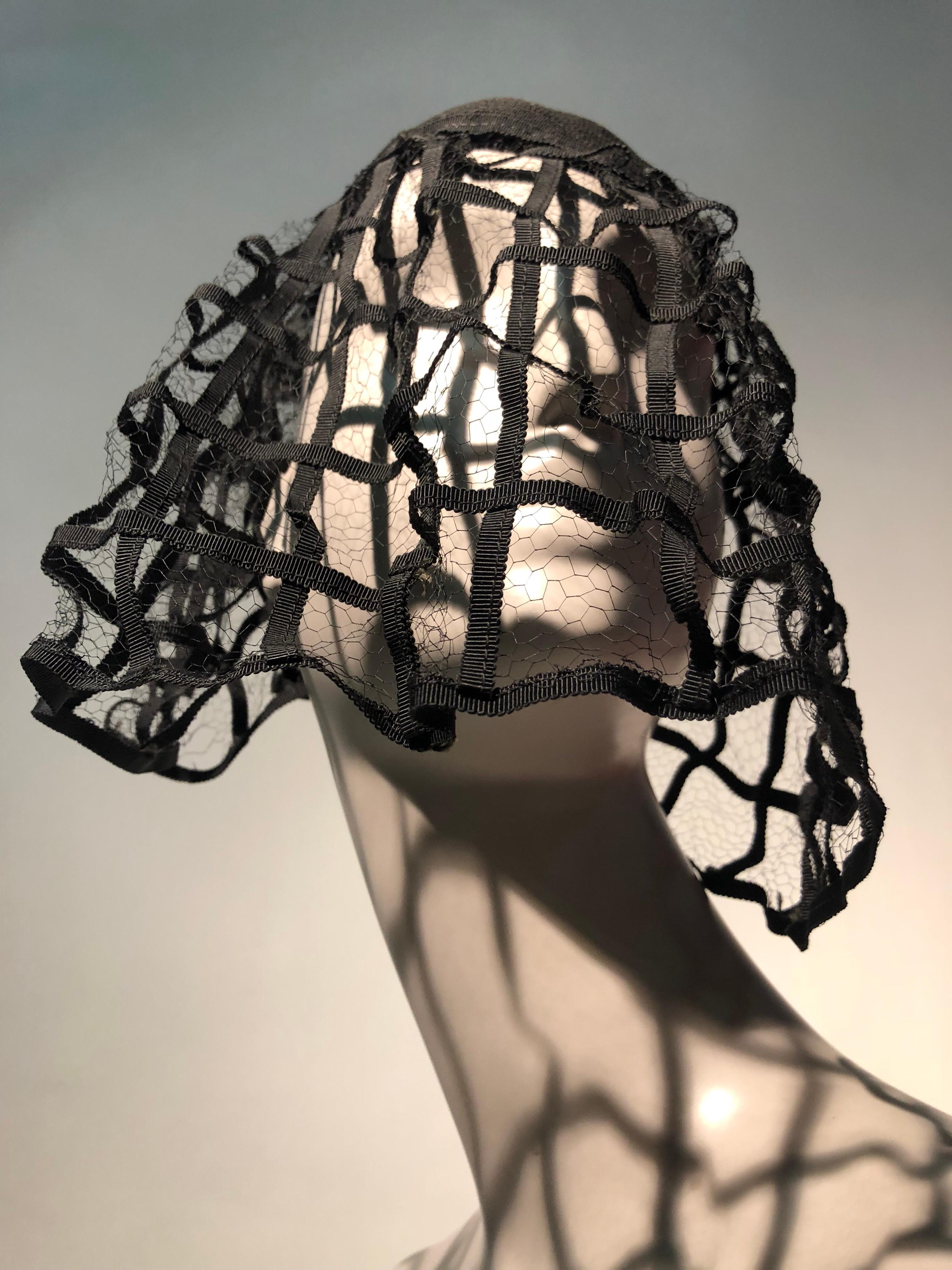 A fabulous, never worn 1940s Hattie Carnegie black hat: made completely of grosgrain ribbon sewn in concentric circles and veiling. The veil is quite interesting and dramatic: A ribbon cage with lighter black veil behind it.  Stunning!  Vintage