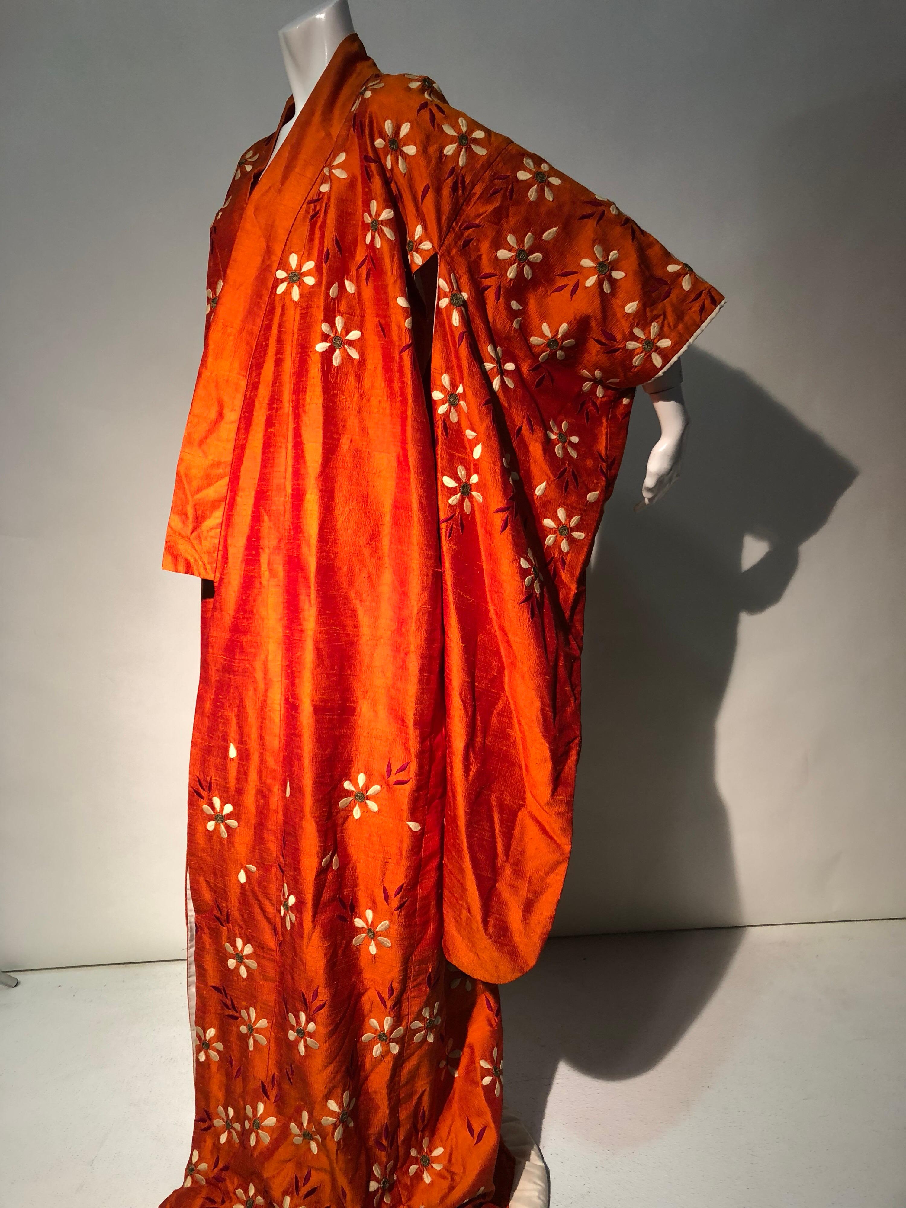 A beautiful 1940s burnt orange raw silk spring kimono with traditional contrasting silk lining, padded hem for train, and silk embroidered daisies throughout. Included is a heavily beaded, adjustable silk belt. Whether lounging at home or making a