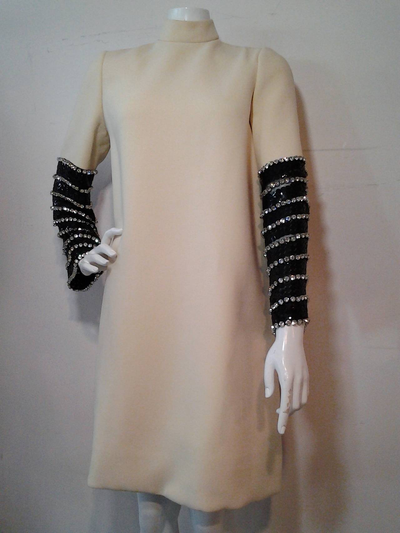 An iconic and spectacular 1960s Norman Norell lightweight ivory wool crepe trapeze shaped cocktail dress with richly embellished sleeve treatment!  Black  paillettes with large prong set rhinestones from mid forearm to cuff!  Fully lined.