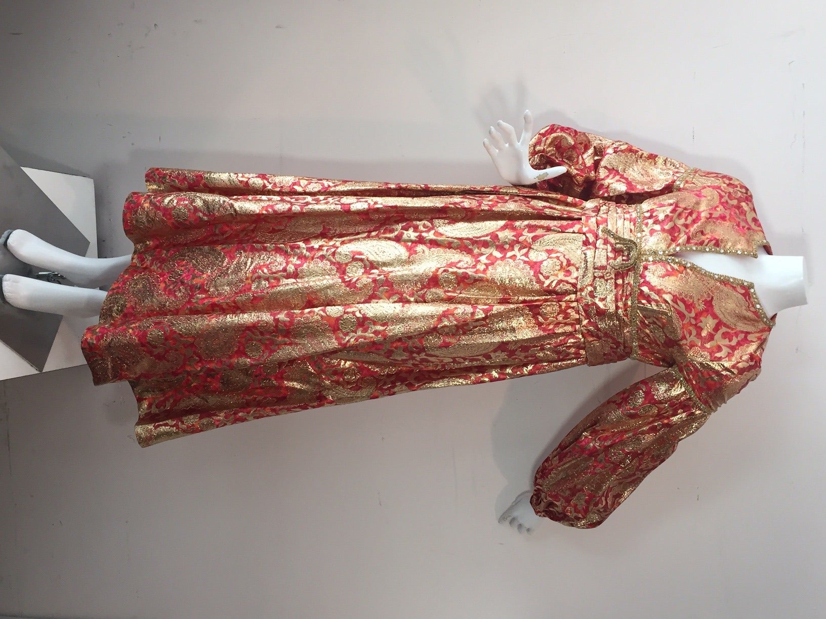 1960s Rizkallah for Malcolm Starr empire waist gown:  pomegranate, coral and gold paisley lame, pleated cummerbund under bust details, full ballooned sleeves and rows of lavish rhinestone trim at neckline, waist and sleeve. Fully lined, back zipper.