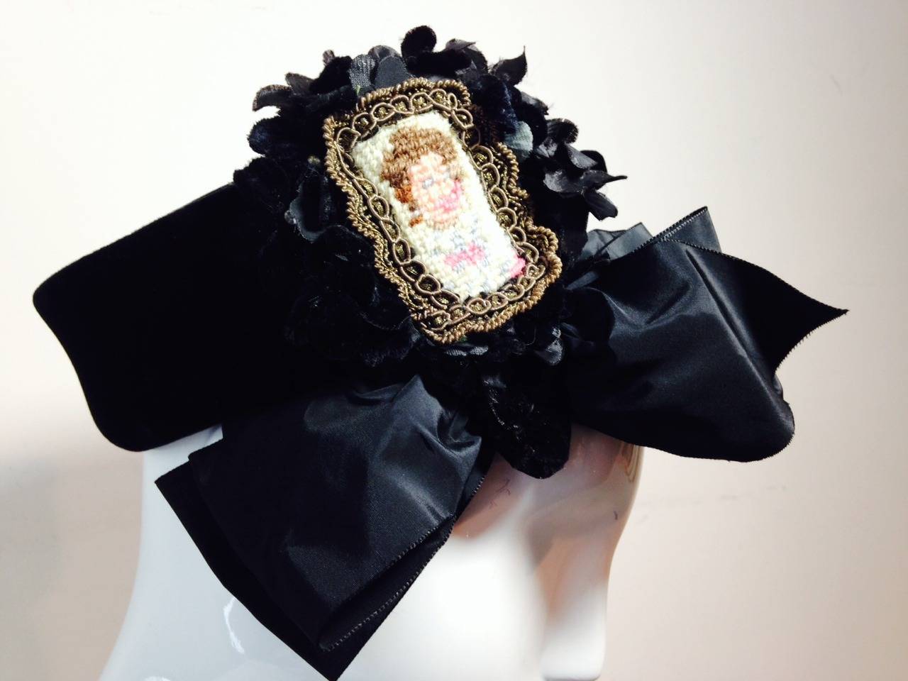 A stunning 1940s Irina Roublon black velvet hat with side embellishments:  black silk flowers, low cheek-bone-skimming  silk satin bow and large needlepoint with gold lame trim and faux cameo.  One size fits all, with combs for attaching to coiffure.