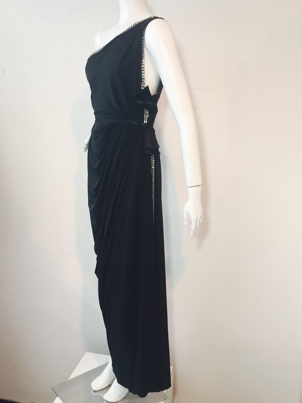 A stunning and revealing 1990s Hall Ludlow Haute Couture evening gown in black polyesther:  One-shouldered styling with scandalously high side slit.  Neckline and side slit are accentuated by a gorgeous heavy line of rhinestones.  Low back