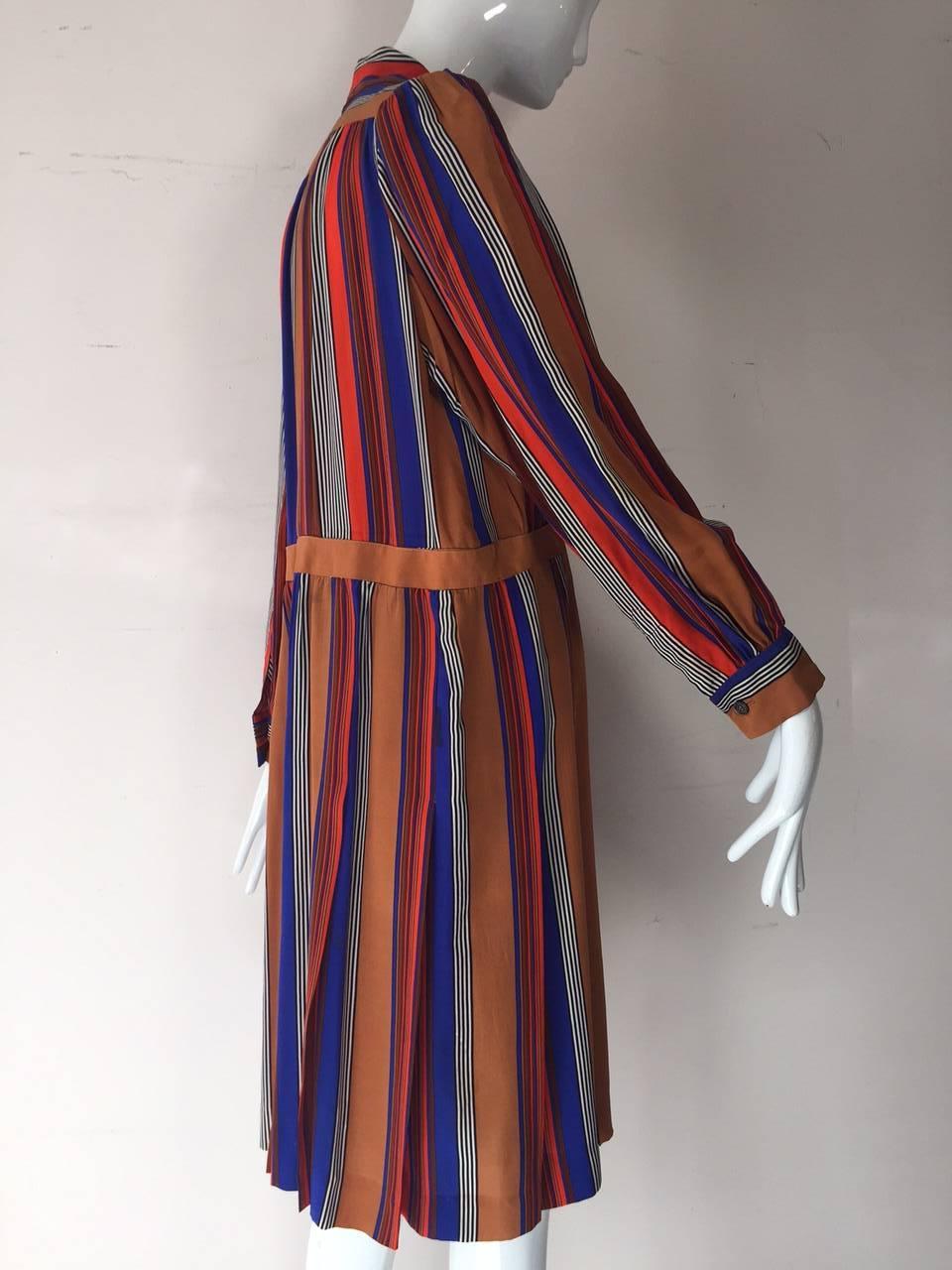 A 1970s Saint Laurent silk striped shirt waist day dress with pleated skirt, button sleeves and attached foulard collar. Red, cobalt, rust and white. Side zip and small shoulder pads. 