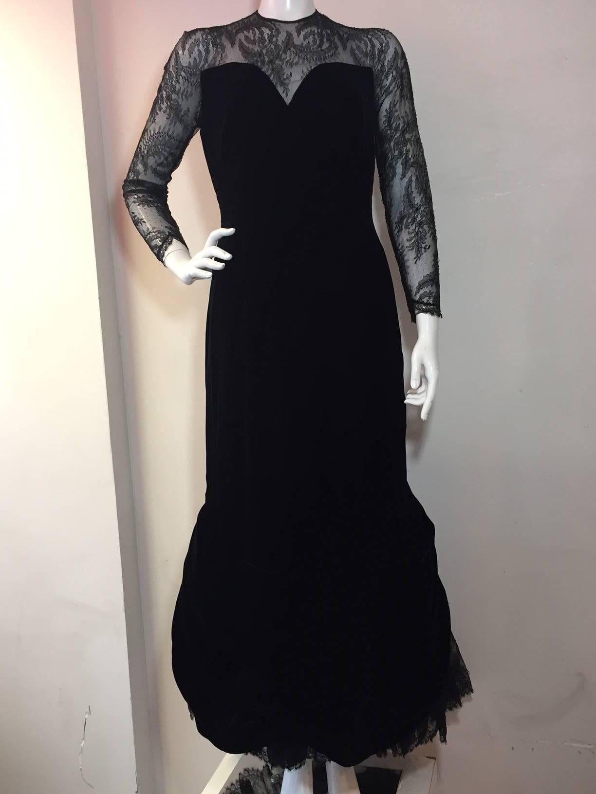 A beautiful 1980s Arnold Scaasi black silk velvet gown with Chantilly lace sleeves, décolletage, and flared inset fishtail train.  The train is voluminous with 8 layers of tulle and horsehair underneath for movement. Two large silk flowers adorns