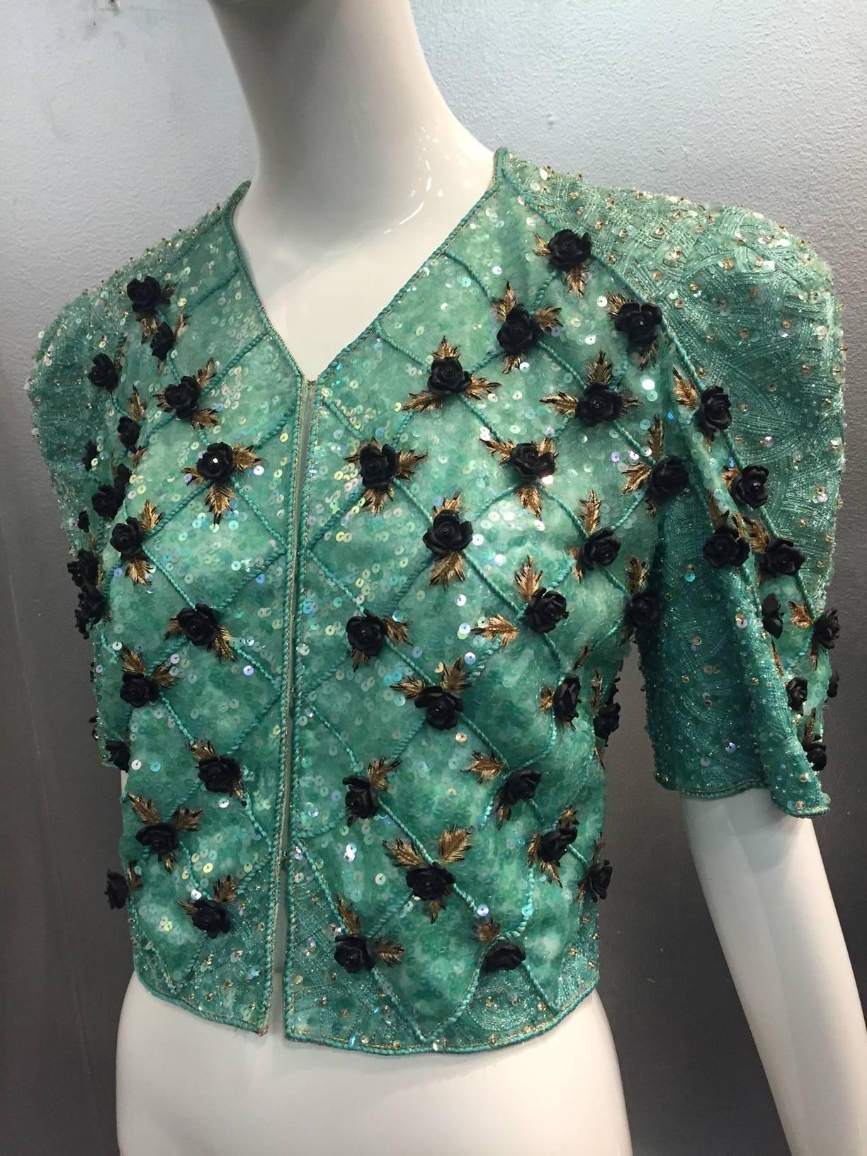 A gorgeous 1980s Carolina Herrera sea foam aqua blue/green intricately bead and sequin encrusted bolero jacket with front hook closure and exaggerated shoulder treatment.  Scattered across the piece, in a trellis pattern, are black resin roses and