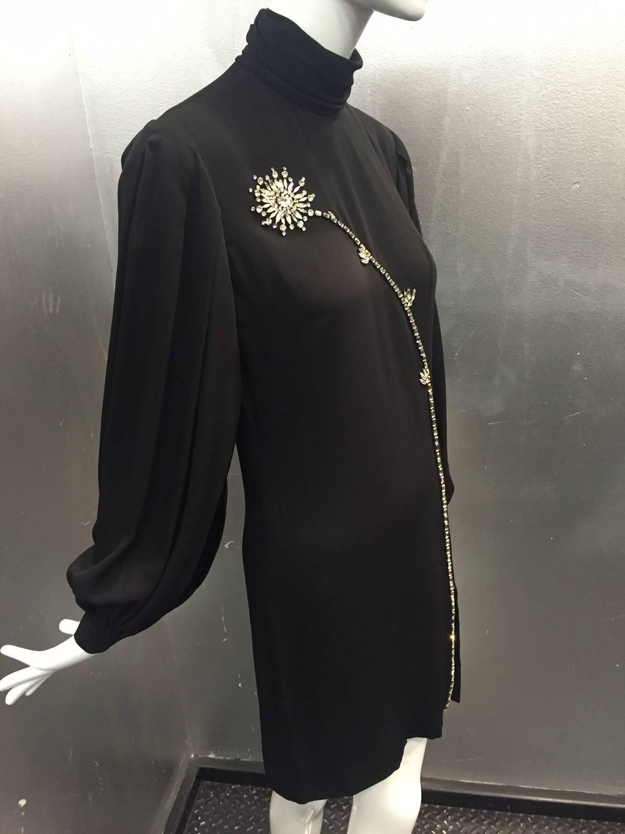 1980s James Galanos black silk crepe mini dress: Funnel neck with back button closure, back zipper.  Pleated shoulder and balloon sleeves. Front side slit is daring with a long stemmed rhinestone flower in front.