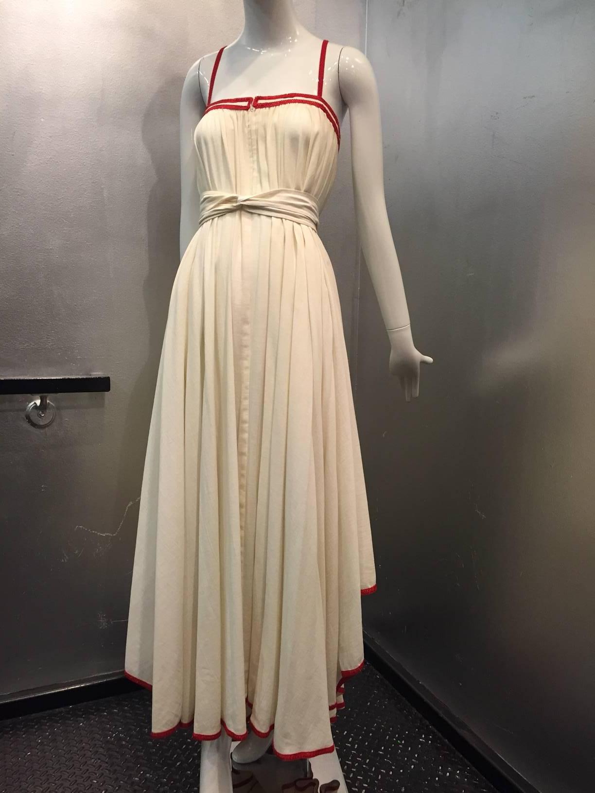 A gorgeous and breezy 1970s Ungaro Parallele natural cotton muslin peasant-style maxi dress with full skirt cut in a free trapeze style (shown with included belt) and can be worn with or without belt.  Front zip. Red braid trimmed straps as well as