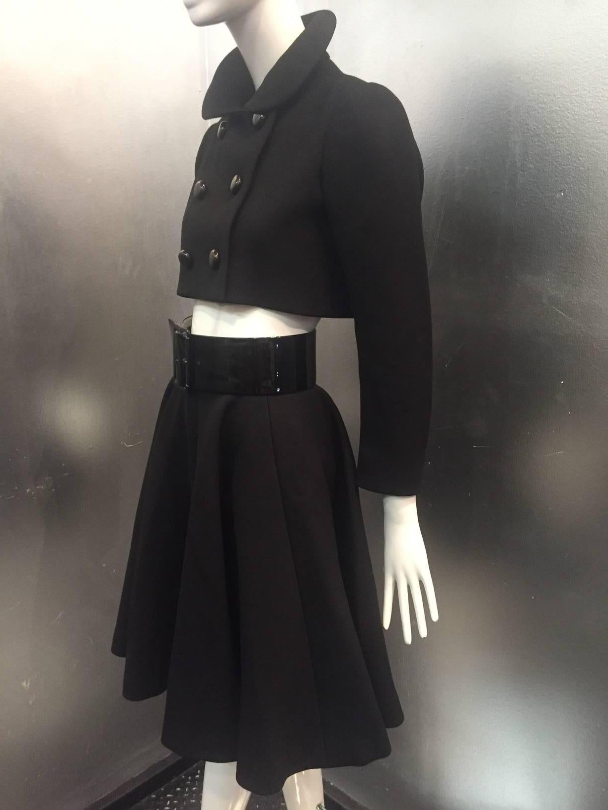 A fantastic 1960s black wool Norman Norell skirt and jacket suit:  Jacket is double breasted with large black bubble-style buttons, cropped short in a bolero style with structured shoulders and Peter Pan collar.  Skirt is flared and full with a
