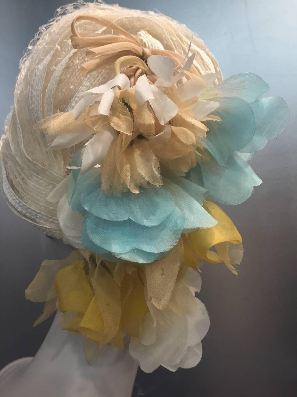 A gorgeous and unusual 1960s Christian Dior off white straw ribbon and net domed turban: Structured interior with grosgrain band.  Back of crown is accented with a dangling tassel of pastel silk flowers in gold beige and blue, and an organza bow. 