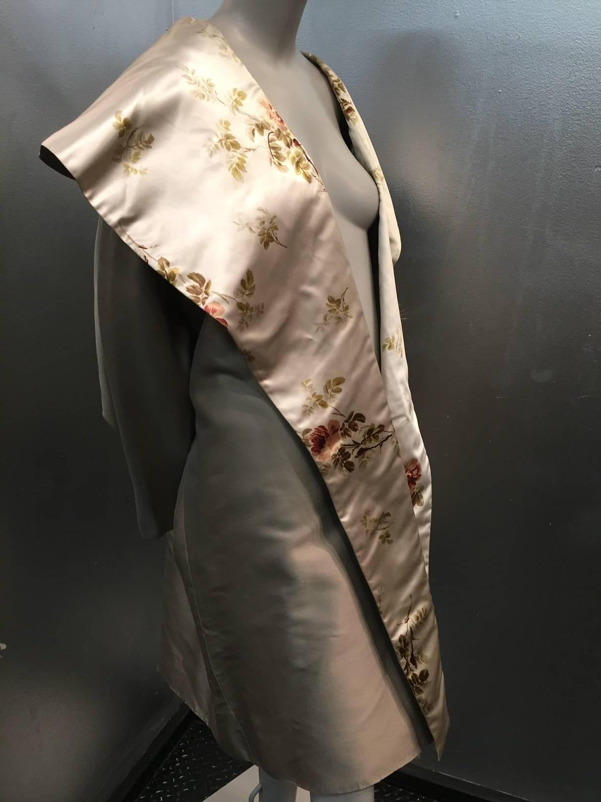 A beautiful 1950s-inspired Calvin Klein dove grey silk satin evening coat lined with a lovely muted pink and green rose print on a champagne background. Large portrait shawl collar.  Intended to be an over-sized cut. No closures. Marked a SMALL but