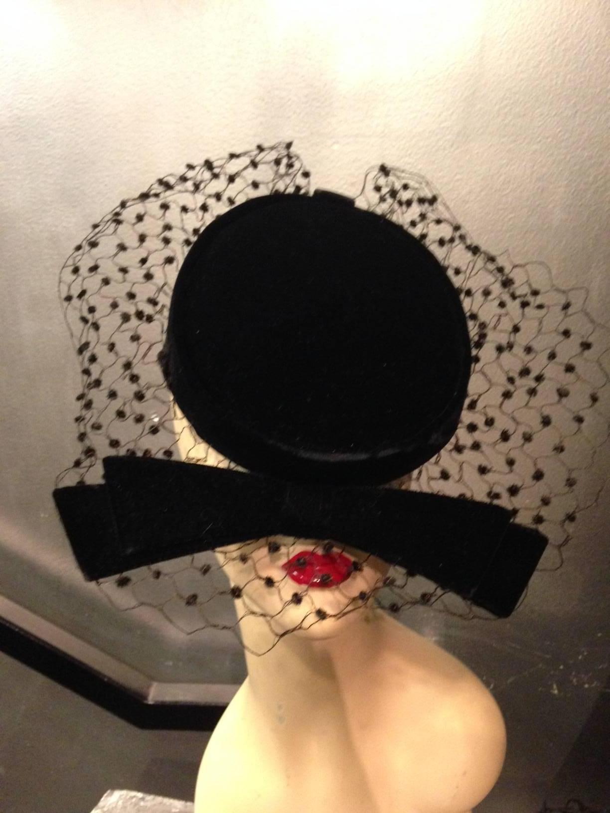 An adorable 1950s Livingston Bros. black velvet cocktail hat with stiff bow and chenille dotted veiling that stands out.  Lined in a pretty floral acetate fabric. 