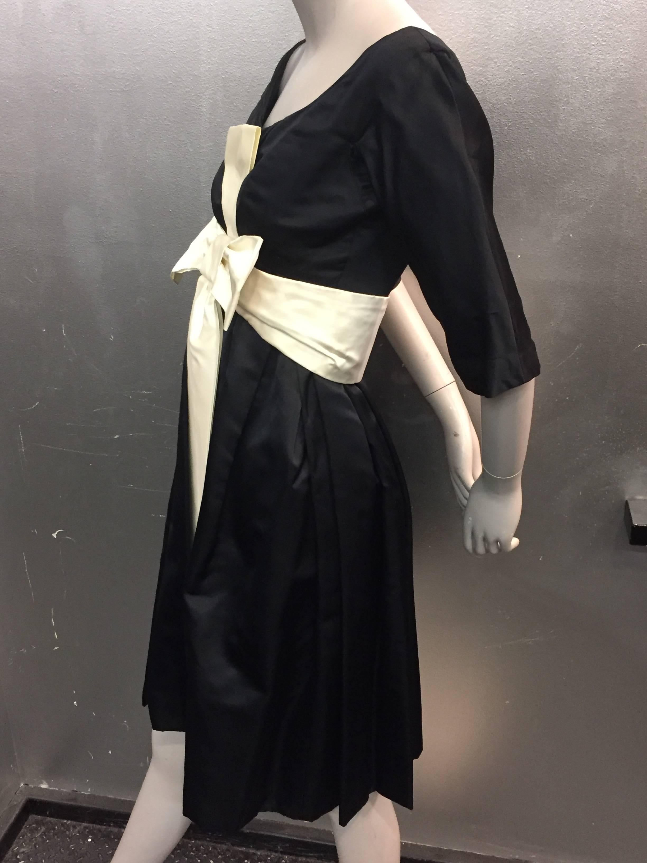 A stunning 1950s Neiman Marcus couture quality black silk cocktail dress:  Scoop neck, 3/4 sleeves, fitted Empire waist line, and pleated full skirt. Leather backed sash/belt construction.