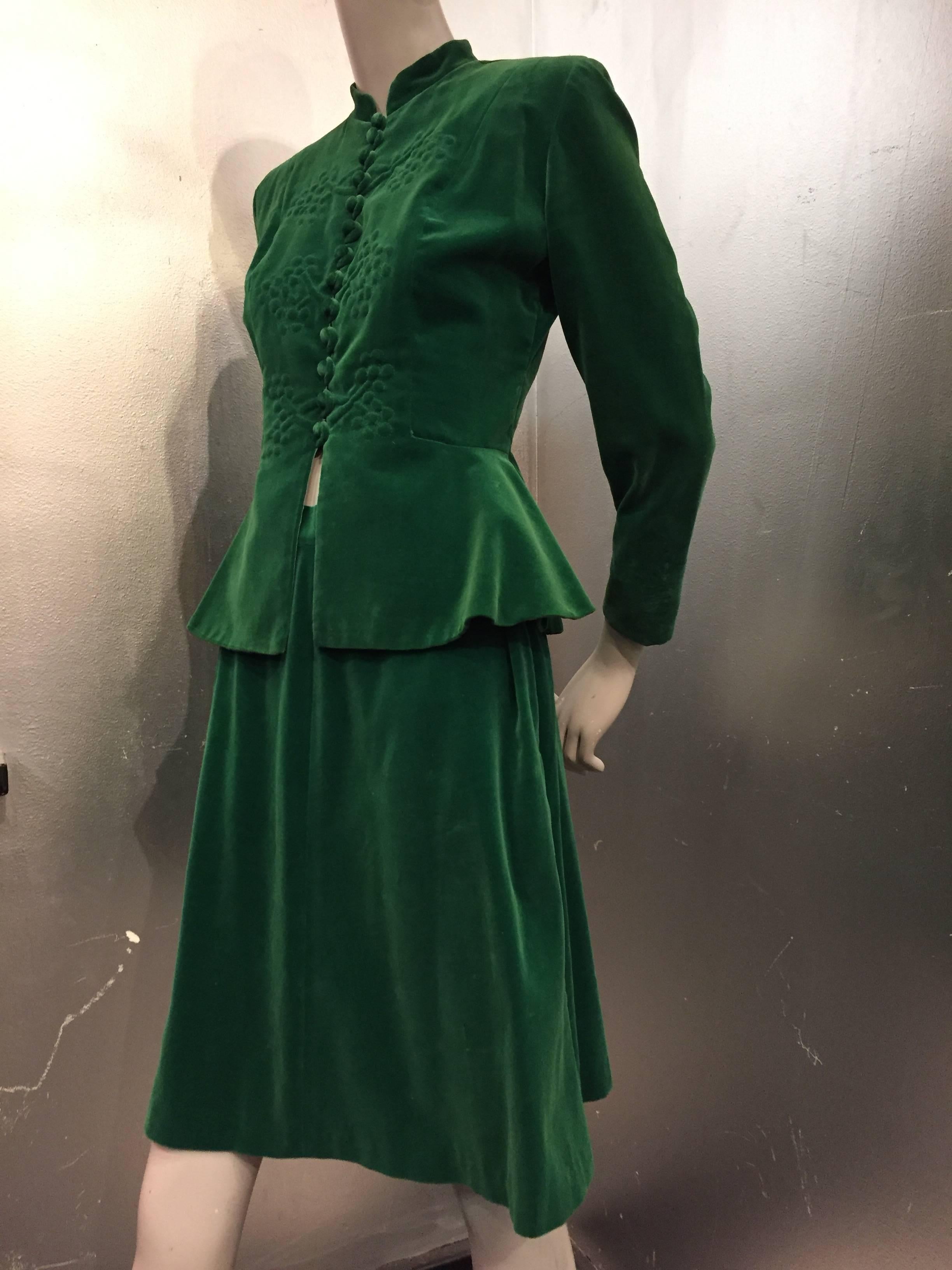 A beautiful and smart 1940s emerald green lightweight supple velvet skirt suit:  Covered buttons and loops down the entire front with beautiful floral trapunto stitch work.  Peplum, Nehru-style collar and tapered sleeves.  Skirt is flared with