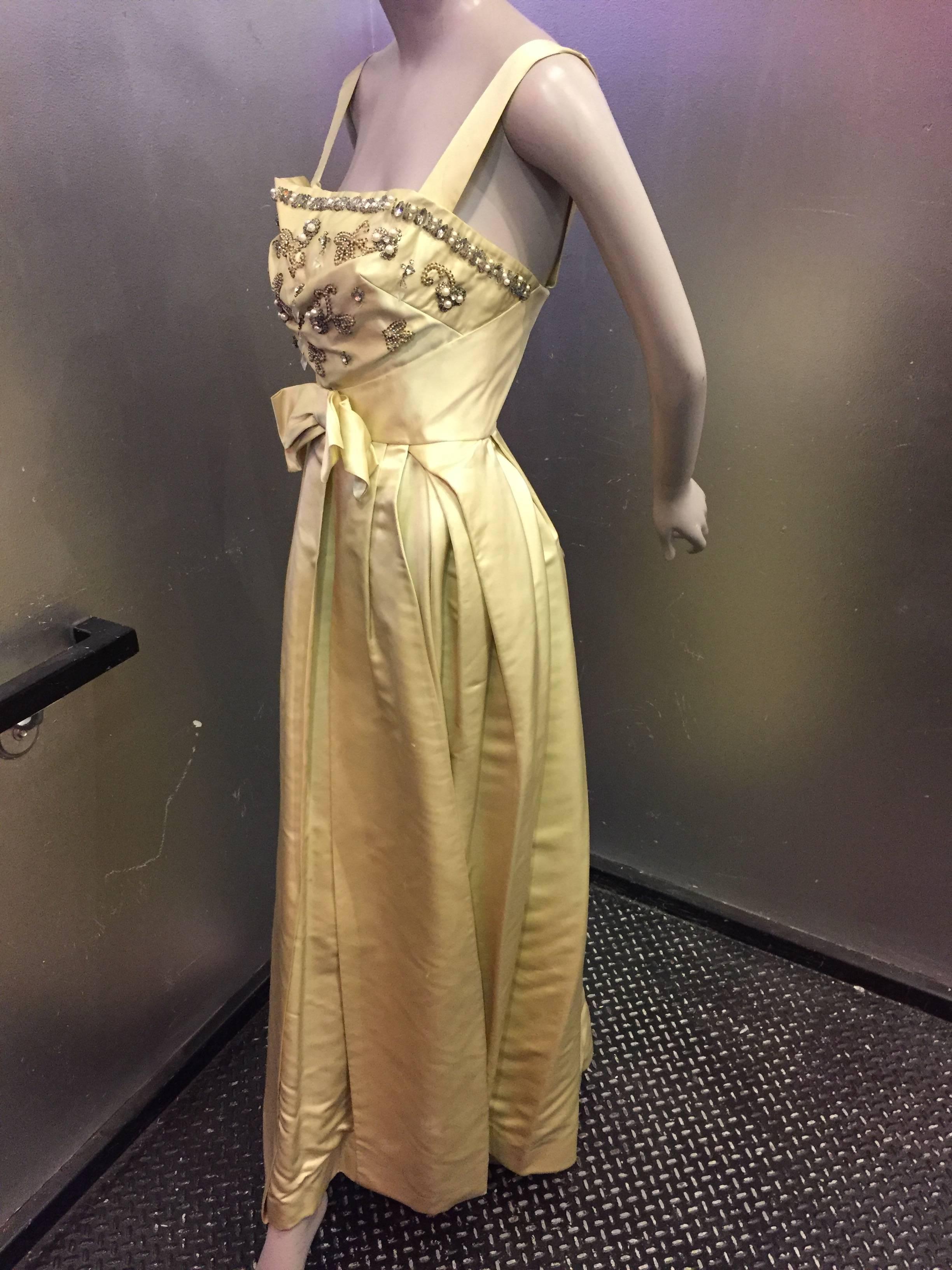 An incredible 1950s celadon silk satin evening gown with wrap-style skirt, fitted waist and a heavily beaded and pearled bust.  Bow and sash panels at center front waist to hem. 