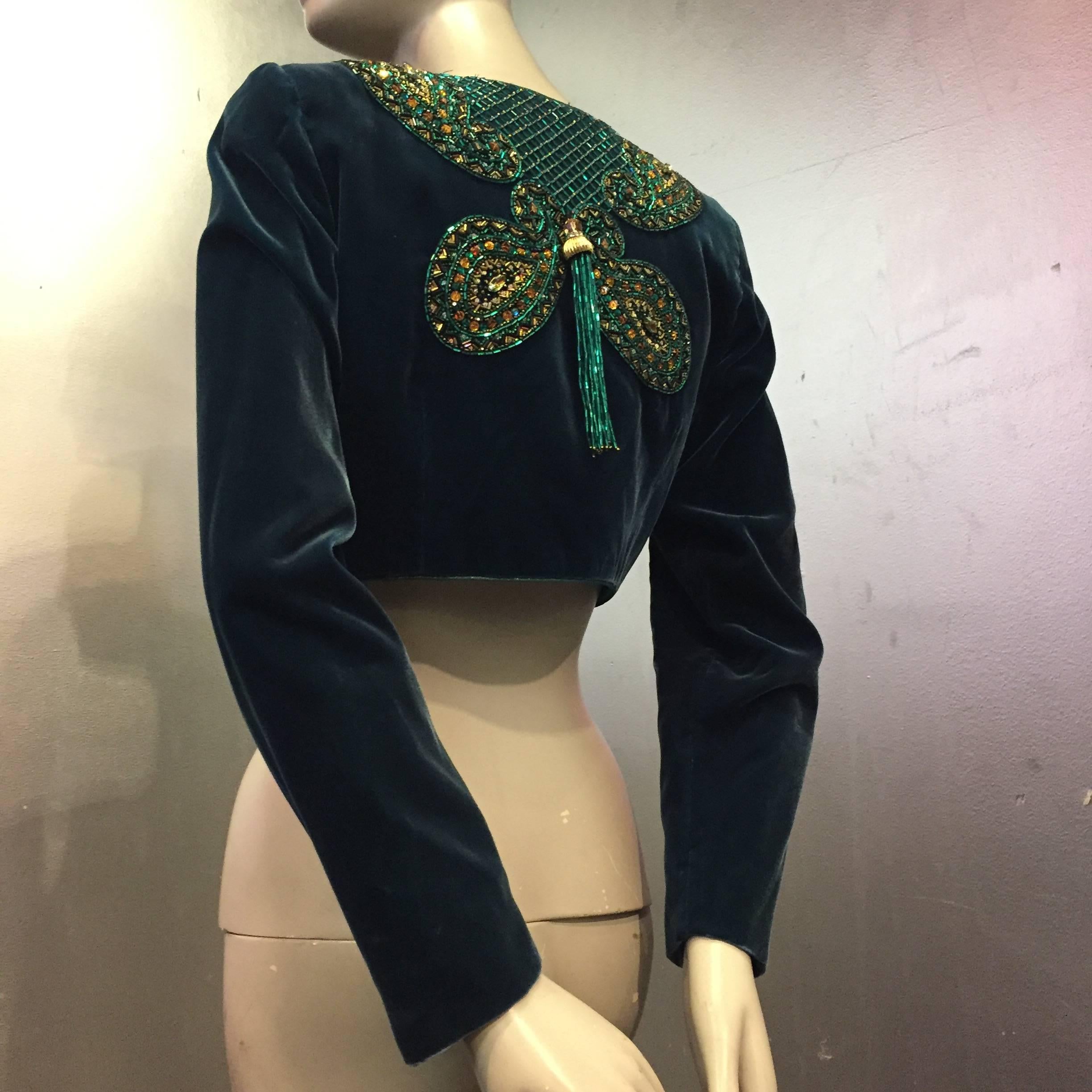 A dramatically beaded silk velvet bolero with turquoise lining. Beaded bodice features a netted pattern with a large beaded tassel by each shoulder. The back consists of a modified cloverleaf motif with a single large tassel at the center of the
