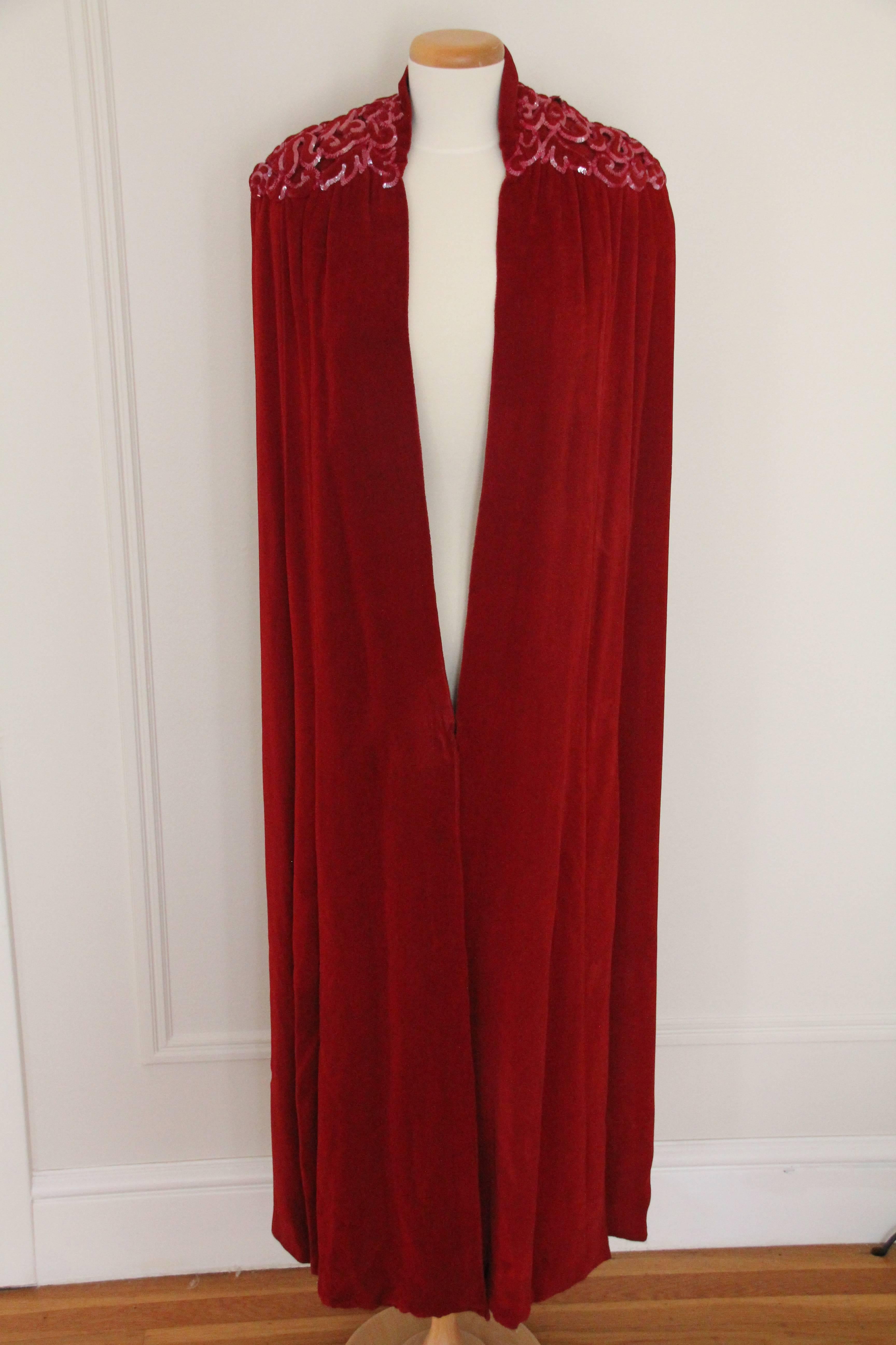A dramatic 1930s crimson velvet couture-style cape with small stand-up collar.  Shoulders are embellished with trapunto-stitched, sequin-edged, velvet cutout detailing. 