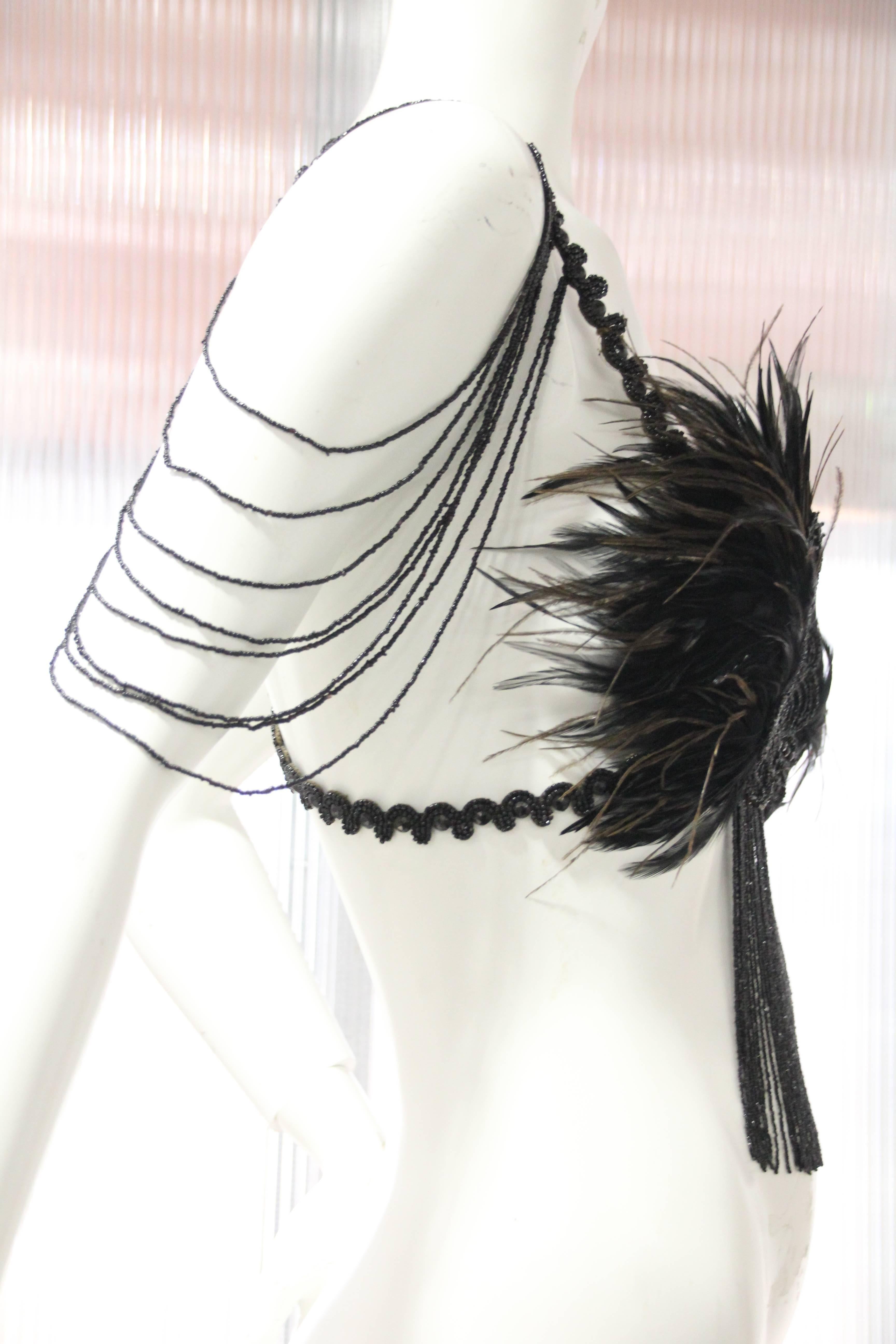 Burlesque bralette constructed of Victorian jet beadwork fringe and feathers. Hook and eye closure at back.  Silk lined cups. Graduated swag beading on shoulders, fringed at center front. All straps are backed with black kid leather. 