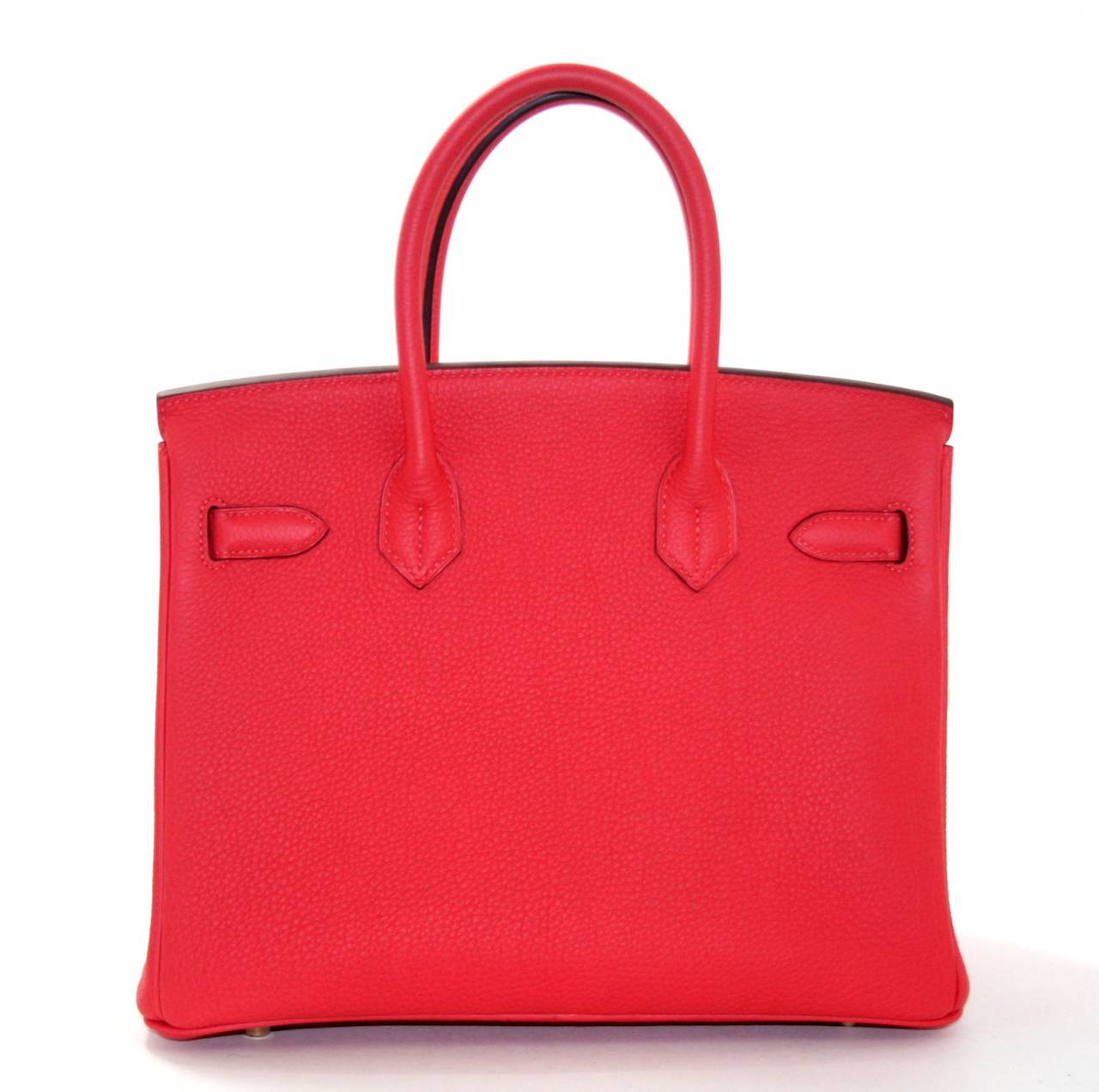 Never carried,  this Hermès 30 cm Rouge Pivoine Togo Birkin Bag is absolutely pristine.  It has been carefully stored with the original felt and the protective plastic remains intact on the hardware.  Considered the ultimate luxury item the world