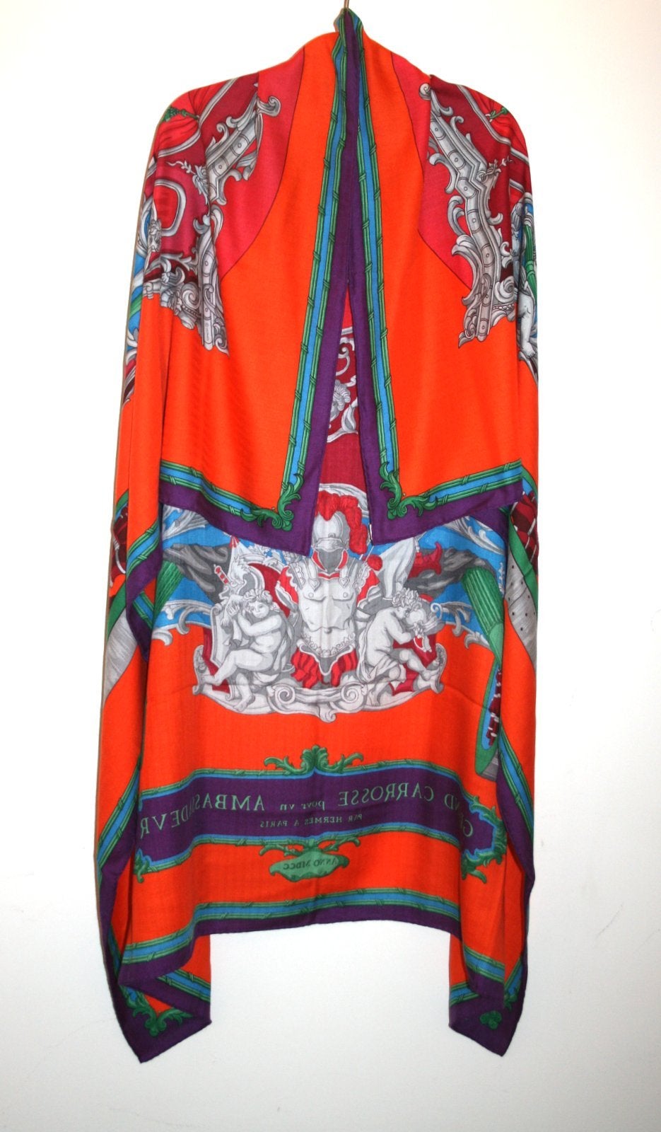 Pristine and unworn with the tag still attached, this Hermès Grand Carrosse Cashmere and Silk GM Shawl is a beautiful collectible.    The Lisa Coutin design features a majestic carriage on an orange red background with accents of purple and green.