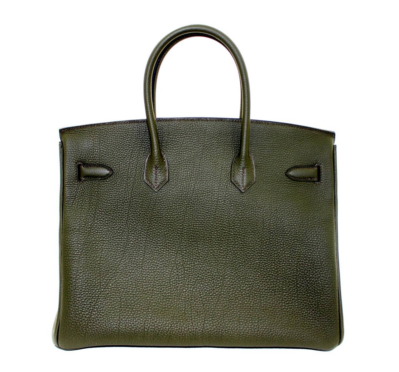 Pristine and never carried, this Hermès Vert Olive 35 cm Birkin Bag has been carefully stored with the protective plastic intact on the hardware.   Considered the ultimate luxury item the world over and hand stitched by skilled craftsmen, wait
