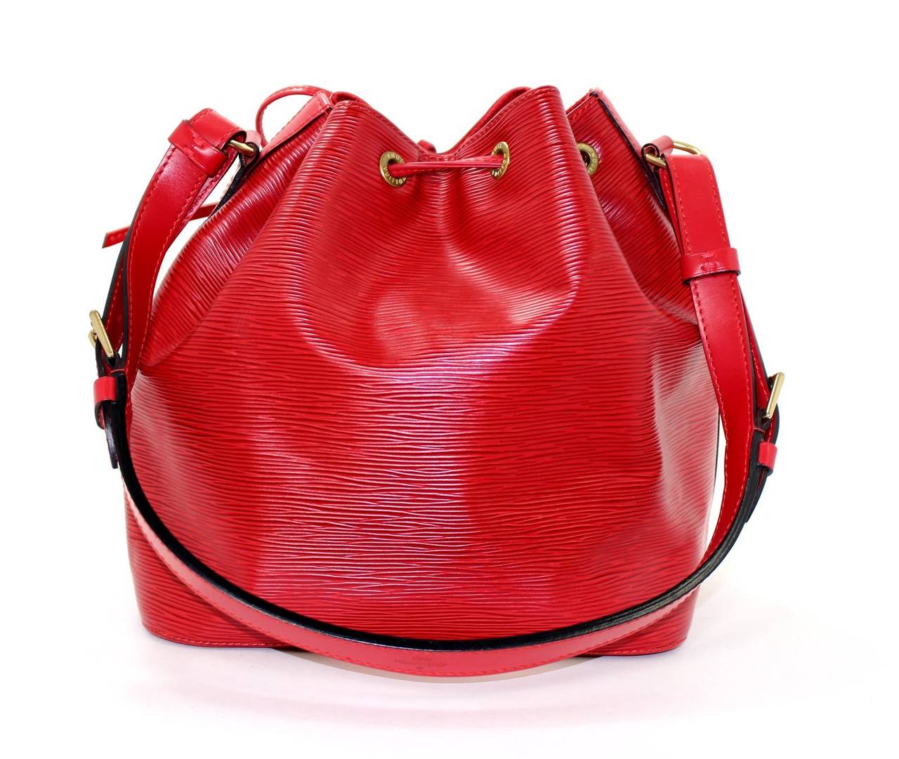 In mint condition, this Red Epi Leather Petit Noe Bucket Bag is a fantastic find with only minor signs of prior ownership. There is a small ink mark on the interior (see photo) and slight hardware scratching.  This is the original version of the