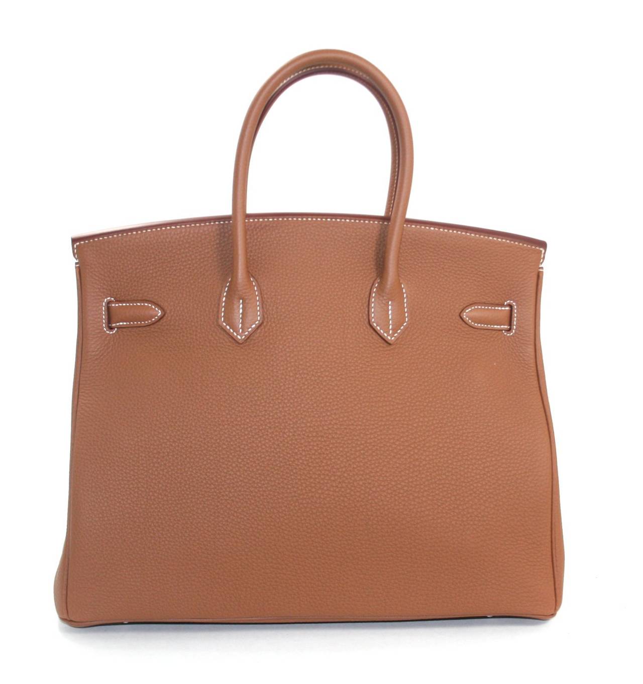 Pristine and unworn, this  Hermès Gold Togo Leather 35 cm Birkin has been carefully stored.  The protective  plastic is still intact on all the hardware.     Considered the ultimate luxury item the world over and hand stitched by skilled craftsmen,