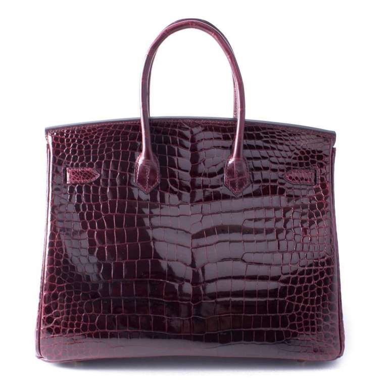 This authentic Hermès Bordeaux Porosus Crocodile 35 cm Birkin has never been carried and remains totally pristine. In fact, the plastic is still intact on the hardware.   Hermès bags are considered the ultimate luxury item the world over.  Hand