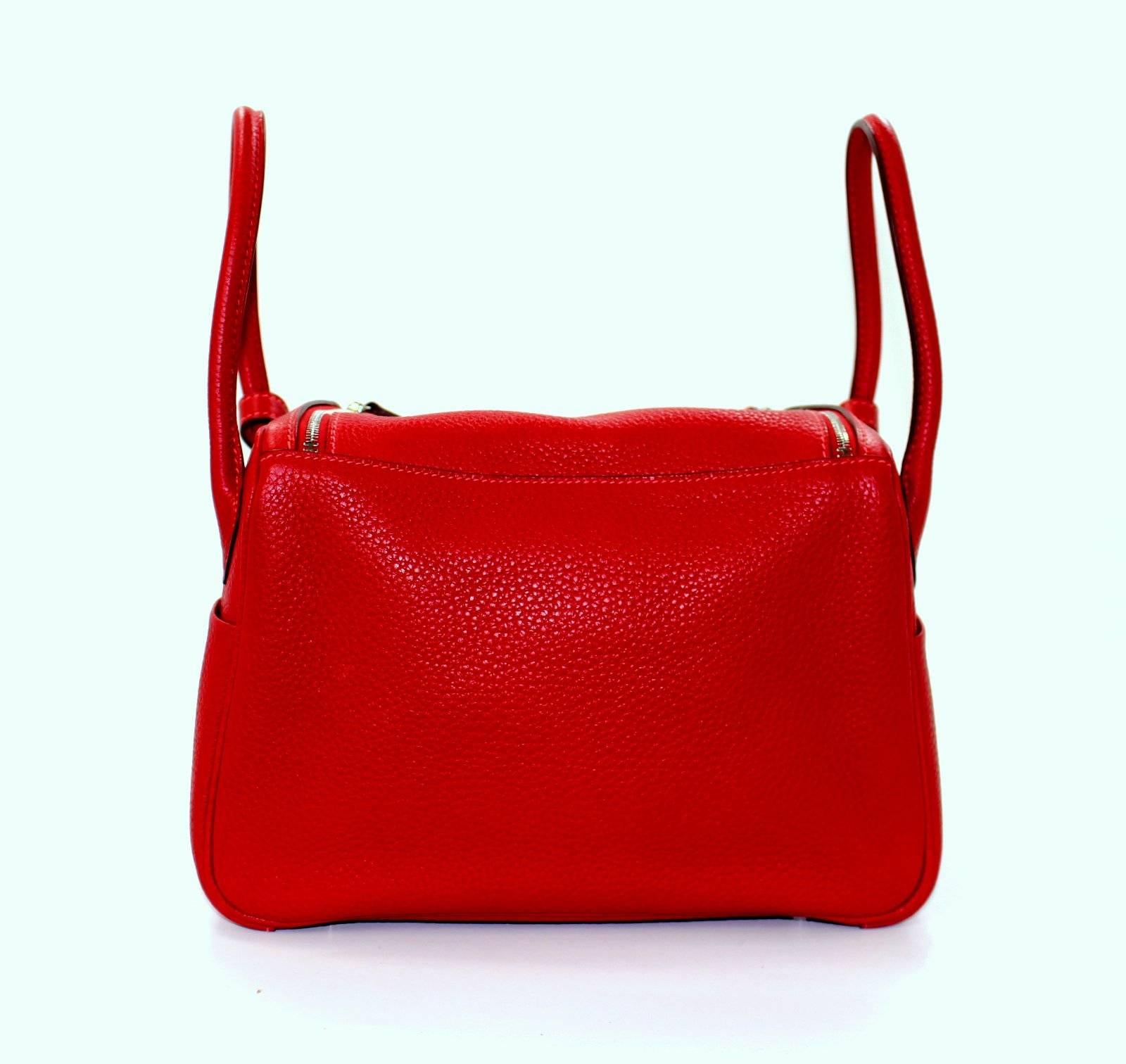 Hermès Rouge Casaque Clemence Lindy 26 cm, PHW- Pristine; Plastic on all hardware except bottom feet

The sporty sister of the Hermès Birkin and Kelly, the Lindy can be carried in hand or on the shoulder.  The slightly relaxed slouch of the