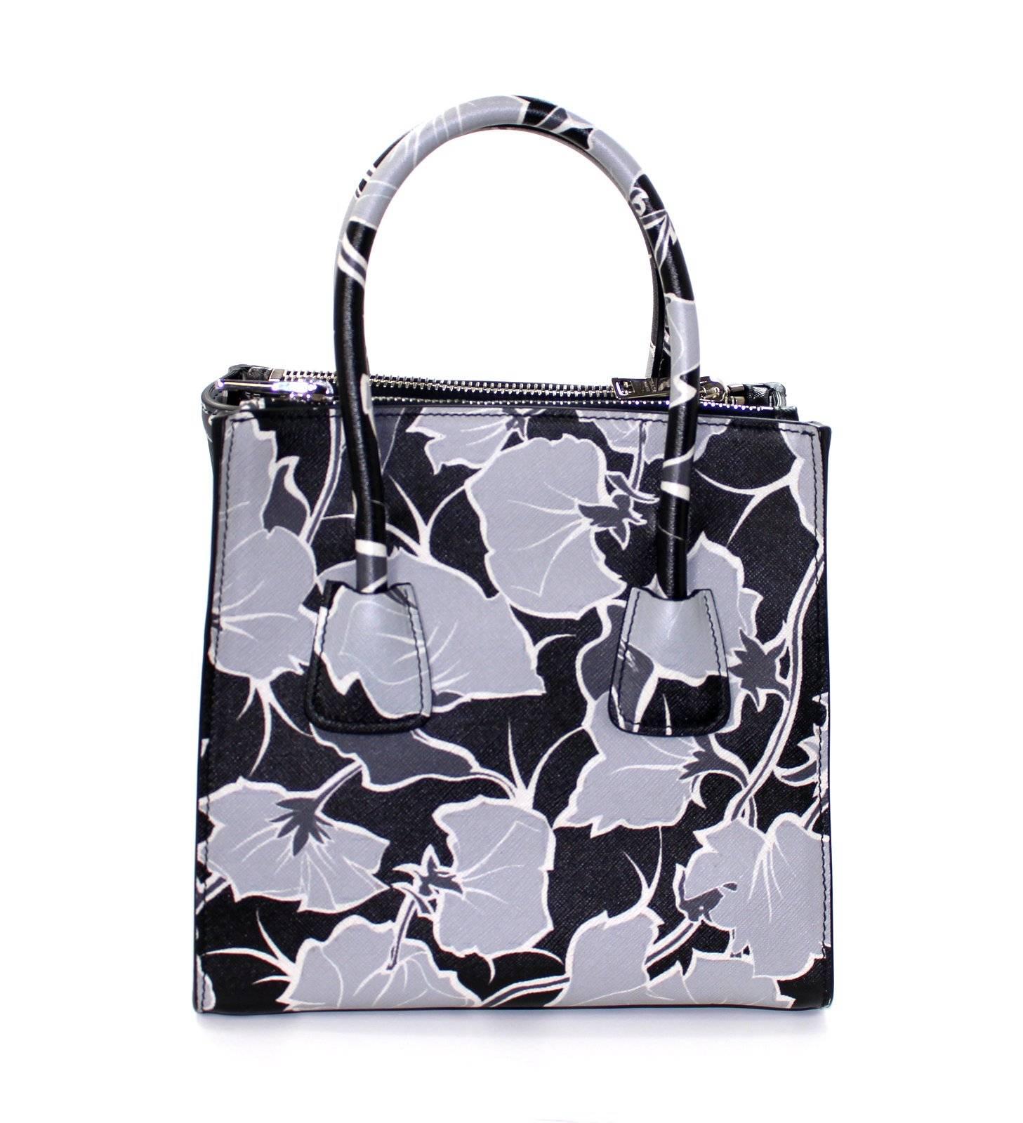 PRADA Grey Floral Saffiano Twin Pocket Tote- NEW, Never Carried!  Estimated current value $2,500.00.
Especially pretty thanks to the unique exploded floral pattern, this Prada also has a variable silhouette with “wings” that may be tucked or flared