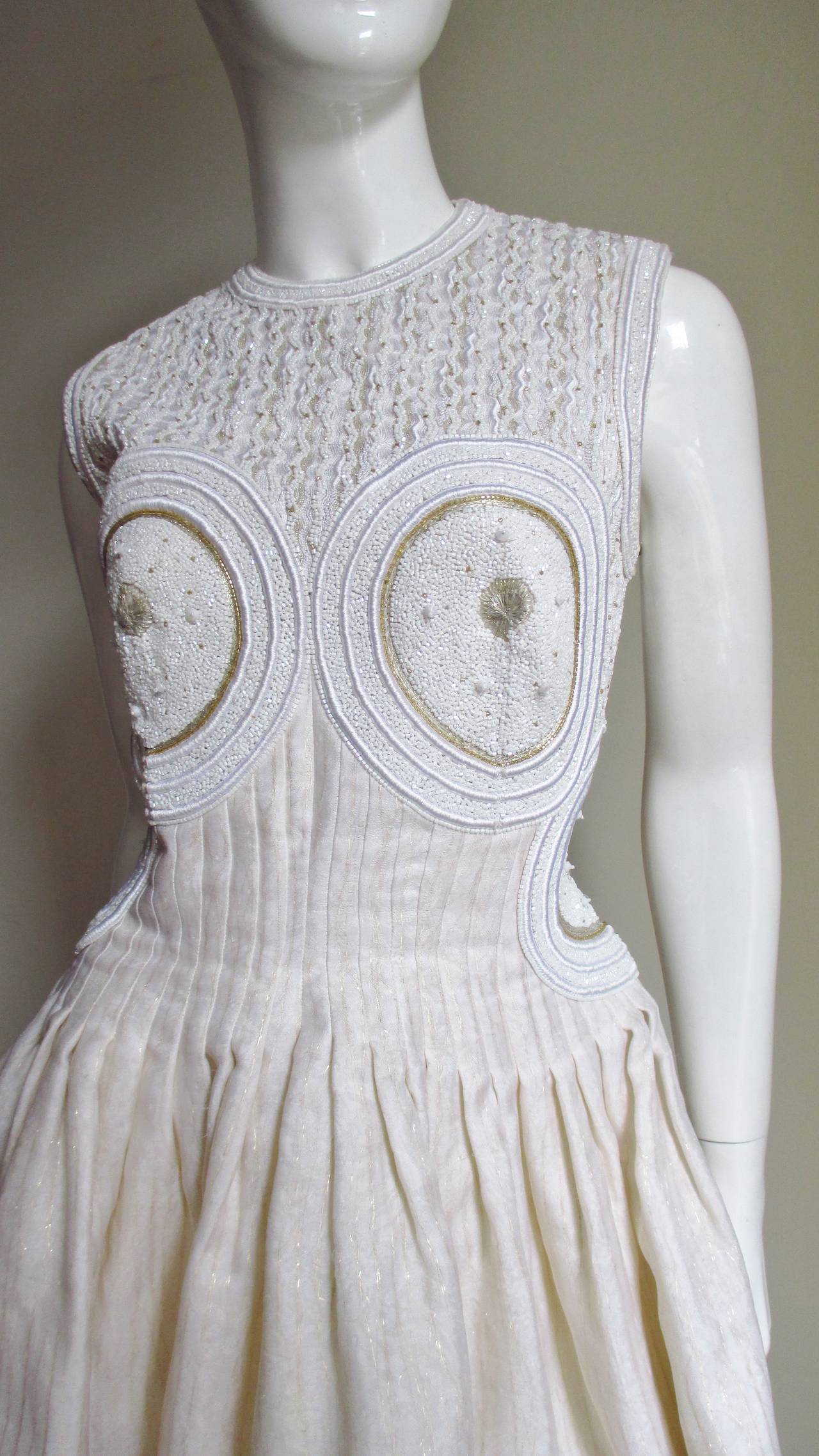 This is one of the more beautifully detailed beaded dresses I have seen- a work of art.  It is made of off white silk shot vertically with gold thread and stunning beading.  The front of the bodice is completely covered in glass beads- lines of tiny