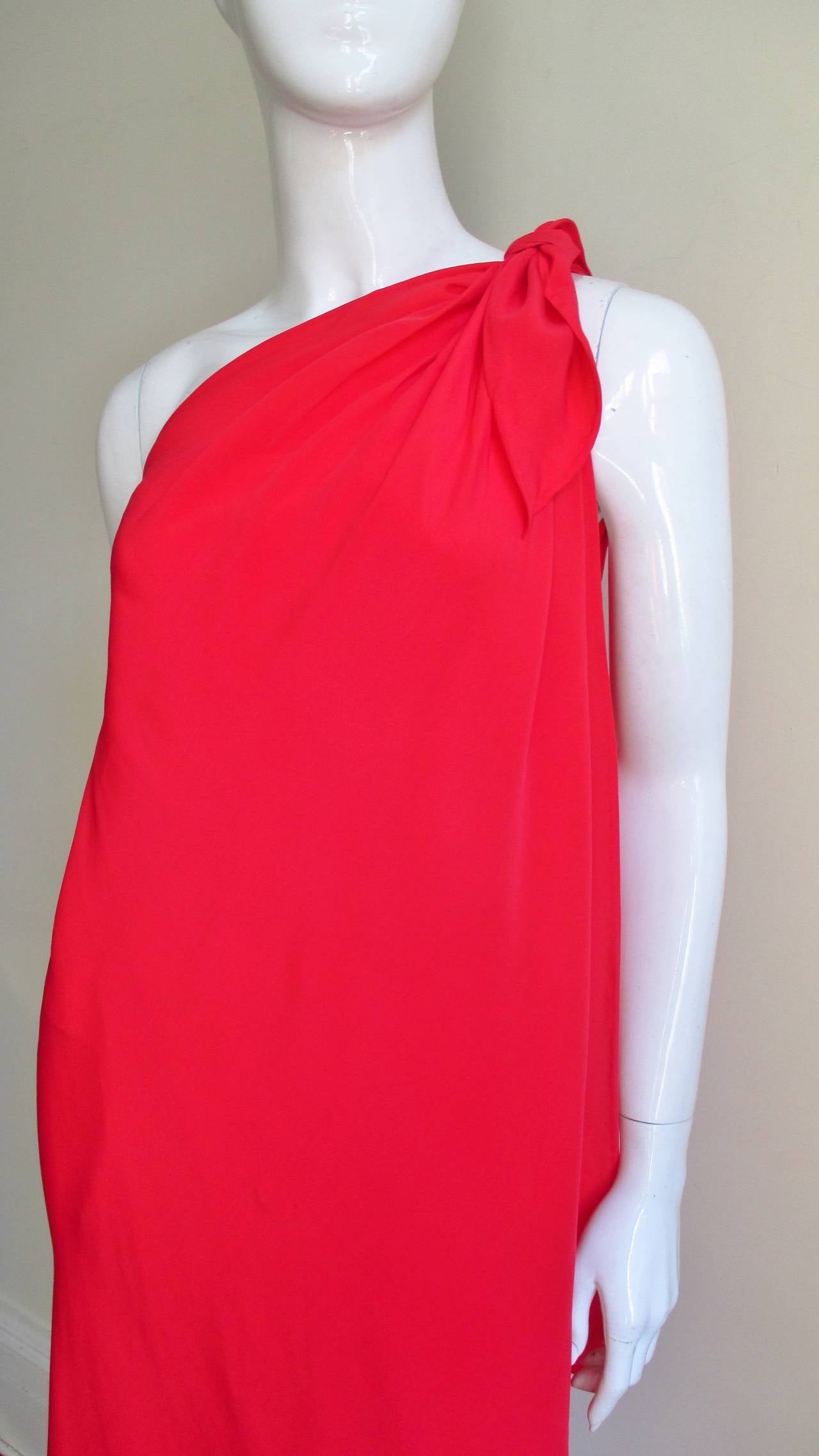 Utter elegance in this one shoulder red silk wrap dress from Halston.  The dress is secured at one shoulder and ties. Then it asymmetrically wraps around the body falling longer in the back crossing at the front at the same angle as the neck to