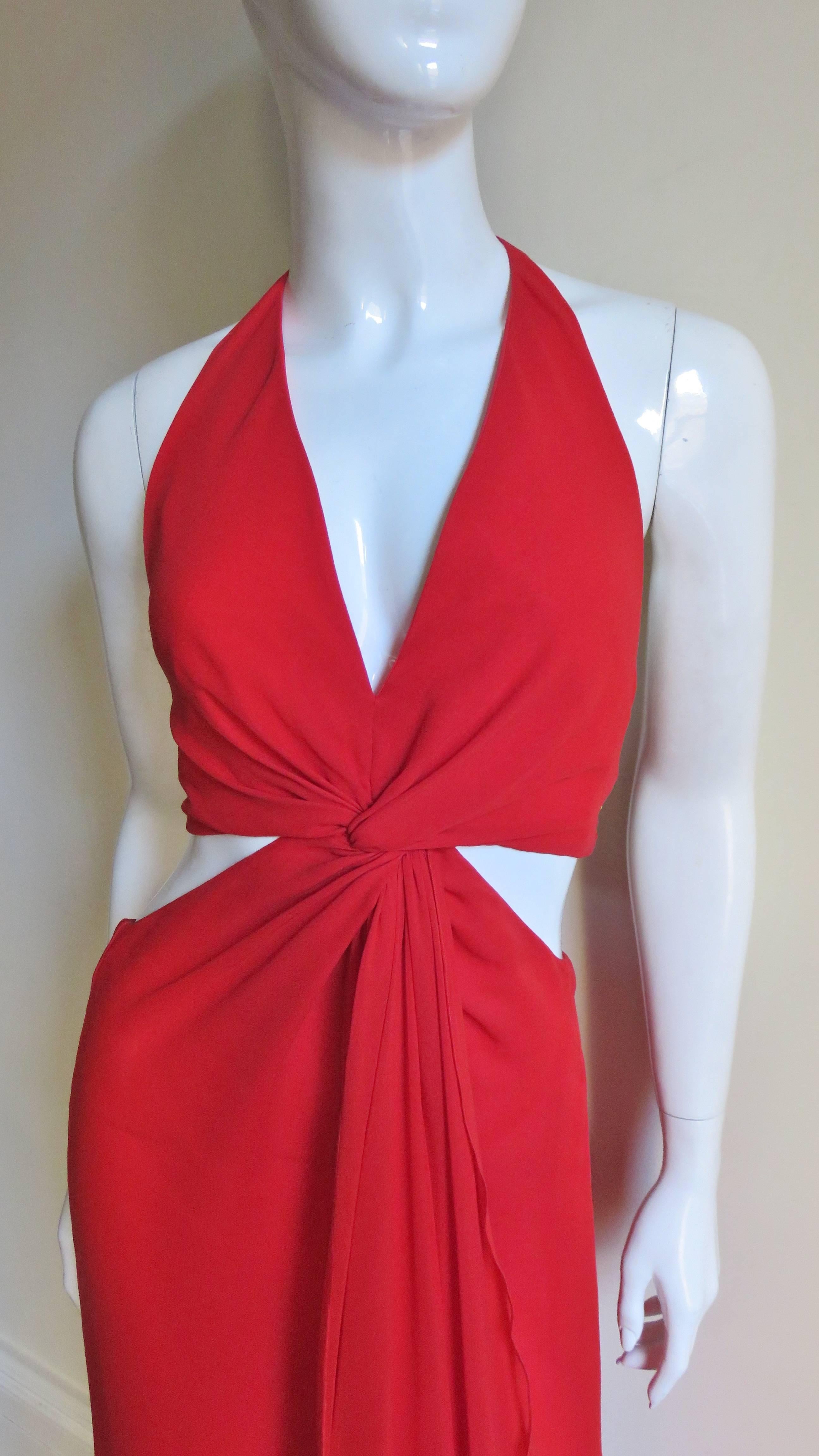 A fabulous red silk gown from Valentino.  It has a plunging halter neckline twisting at the center front with a low cut to the waist back with a cross strap at mid back.  The sides are open above and below the waist.  There is a center front skirt