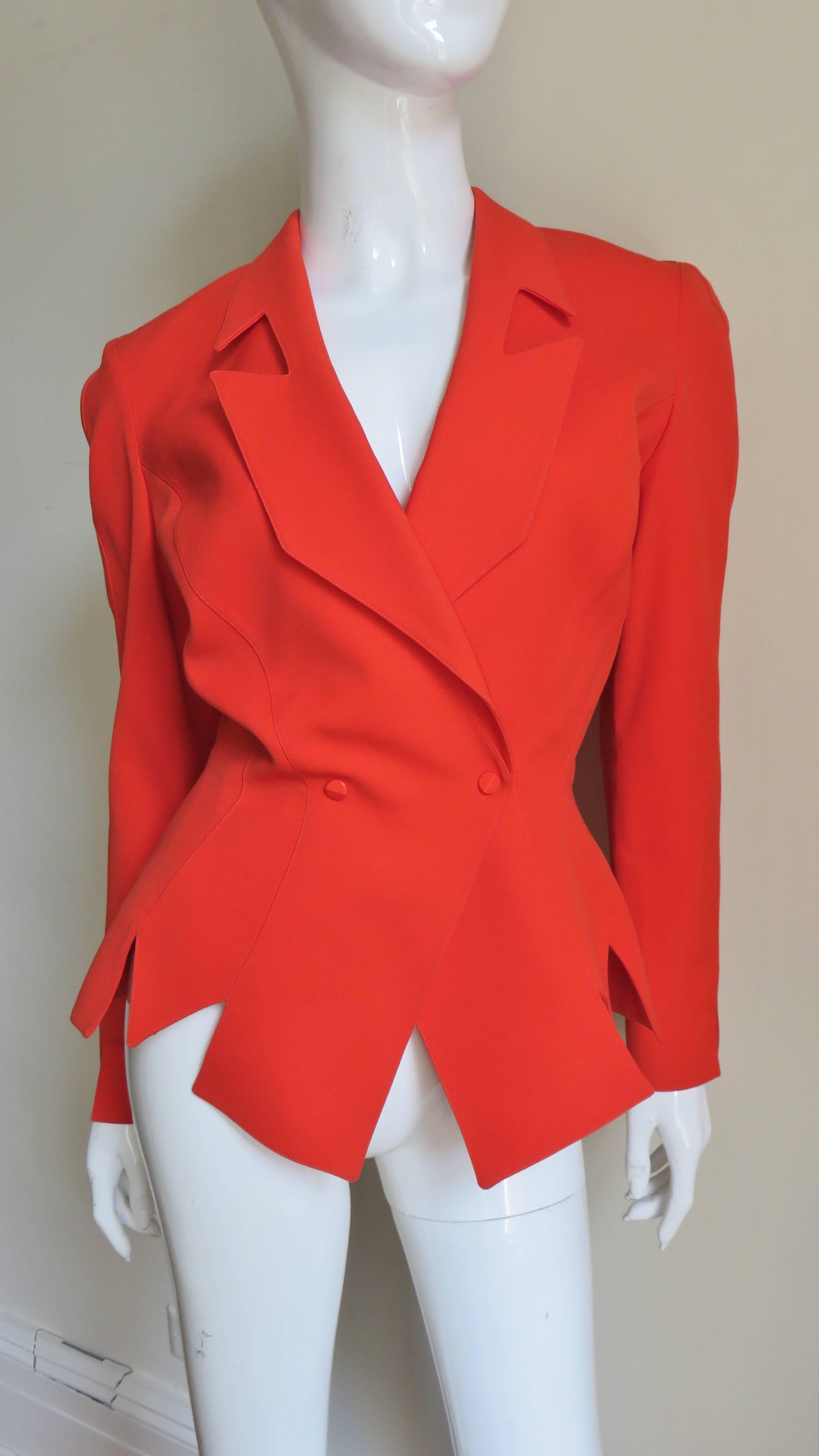 A great bright orange jacket jacket from Theirry Mugler.  It has a cutout lapel collar and has multiple length wise seaming creating a cinched waist.  The sleeve cuffs have cut out points as does the bottom of the jacket.  It is fully lined in