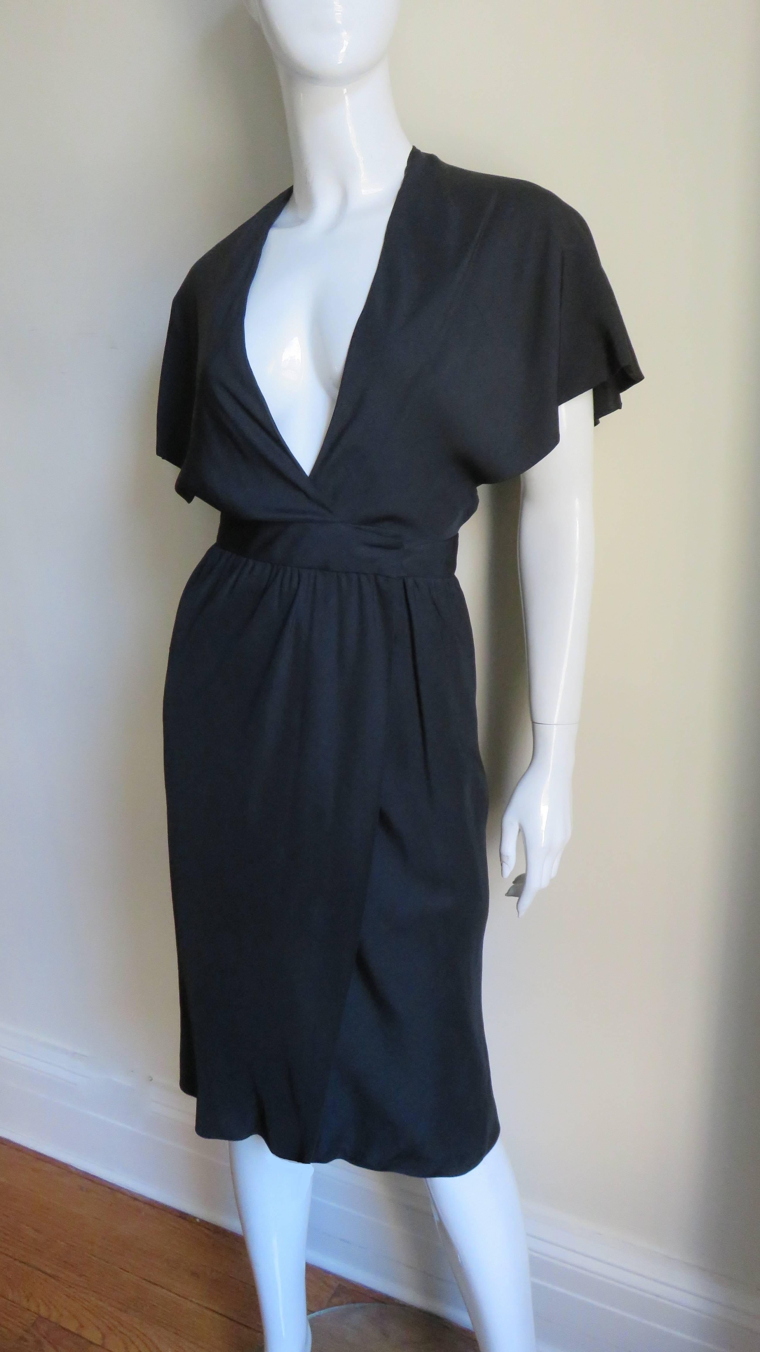 A beautiful black silk dress from Halston. It has a plunging neckline, cape sleeves and wraps at the front waist. The skirt portion is straight gathering onto a waistband which hooks closed at the side waist. It is fully lined in black silk and has