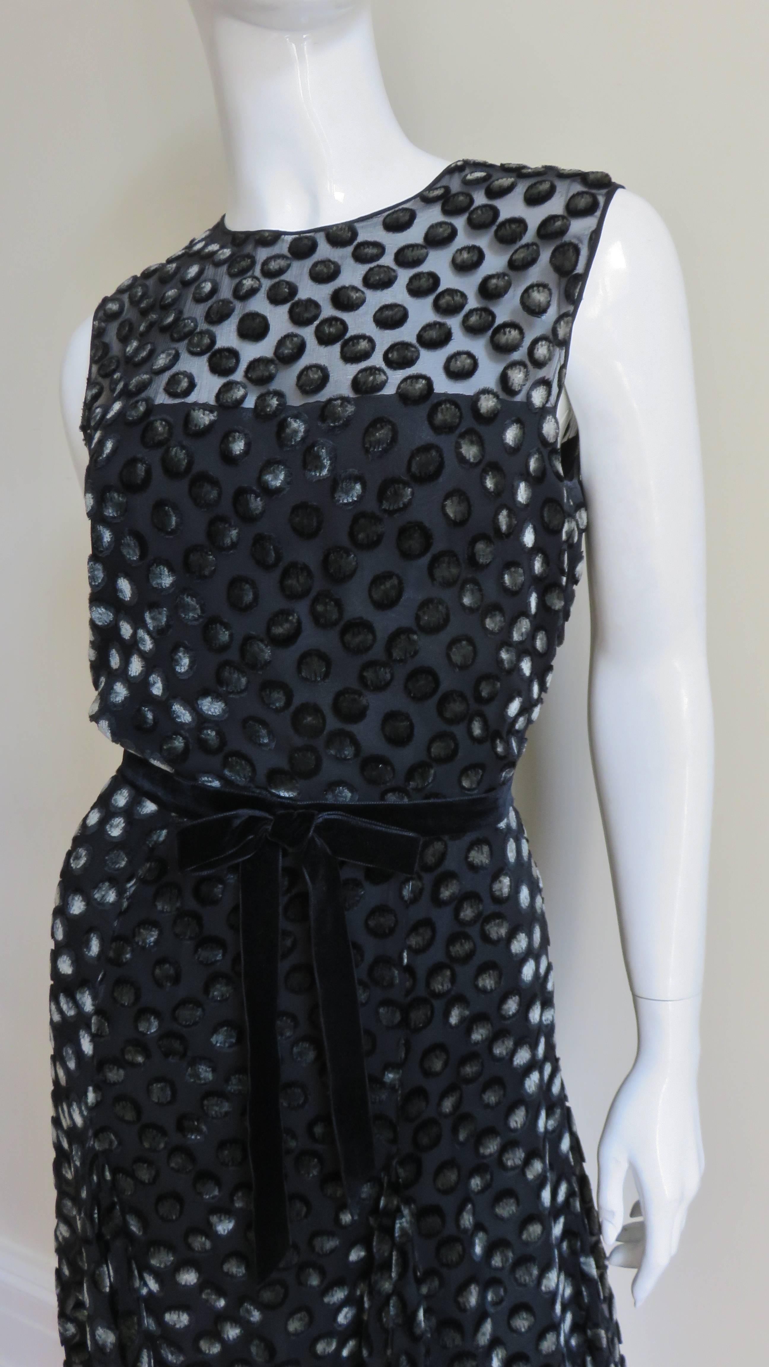 A beautiful black semi sheer silk dress by Bill Blass covered with black velvet dots with grey centers. It is sleeveless with a crew neckline, a blouson bodice with a black velvet belt at the waist and a full skirt.  The dress has a silk lining