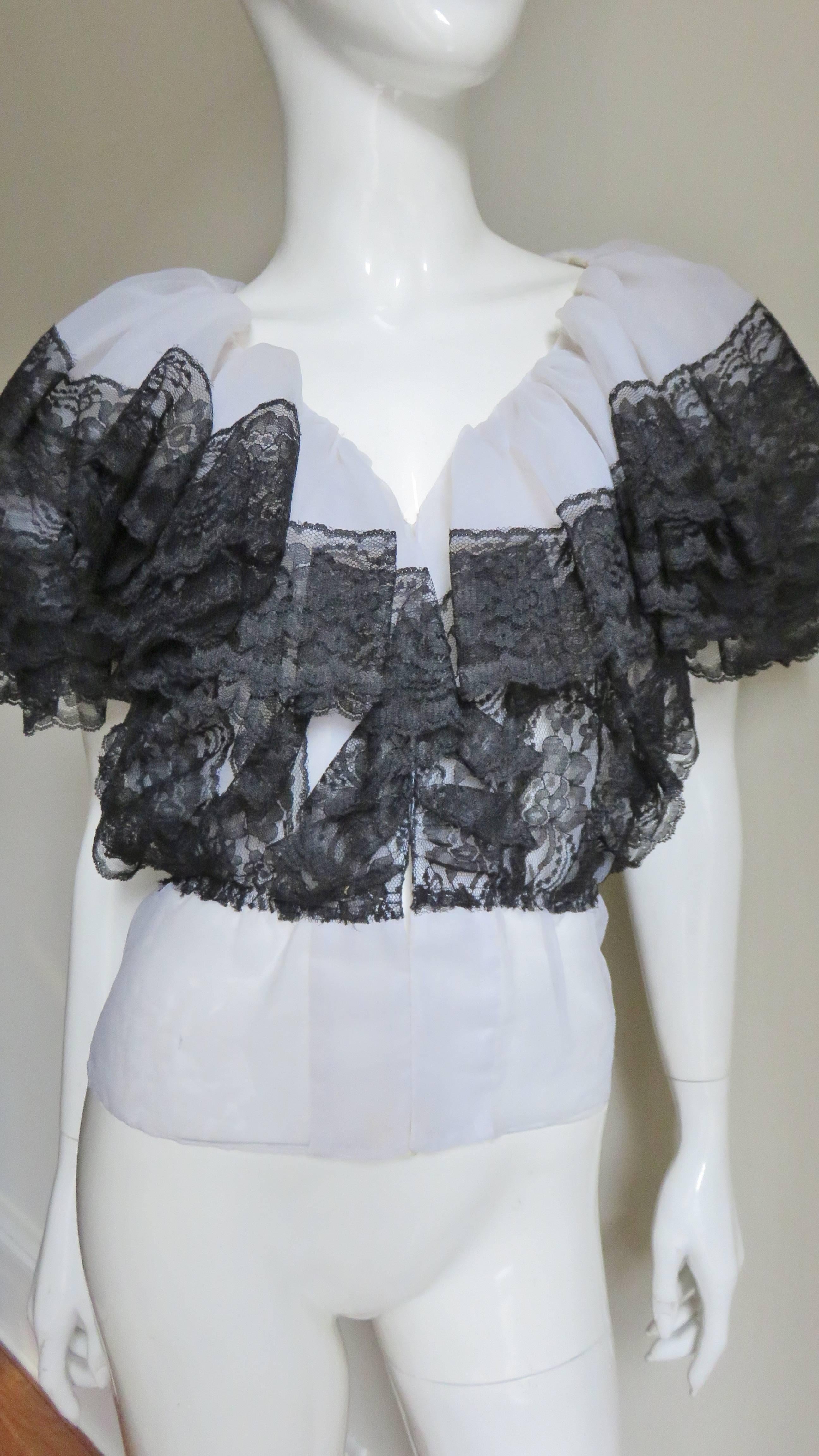 A gorgeous white organza and black top by Mignon.  It is V neck with a double layer gathered organza collar which lays over top cape sleeves all edged in 3" black lace with a scallop hem. The torso has vertical row of the black lace attached to