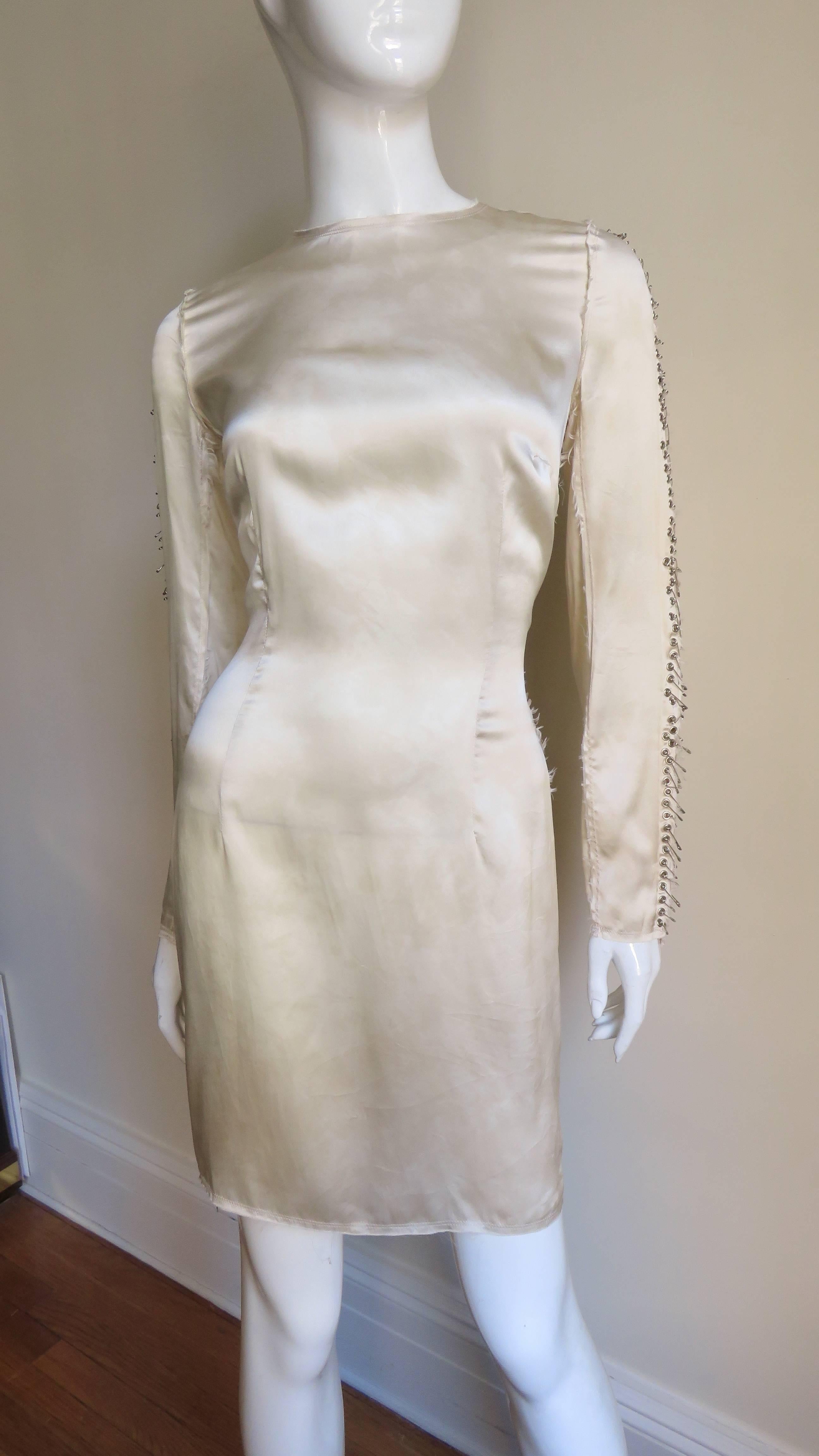 A beautiful pale yellow silk dress from Pierre Balmain.  It is semi fitted skimming the body with a crew neckline and long sleeves adorned along the outside with dozens of silver safety pins of varying sizes. The dress strikes a deconstructed note